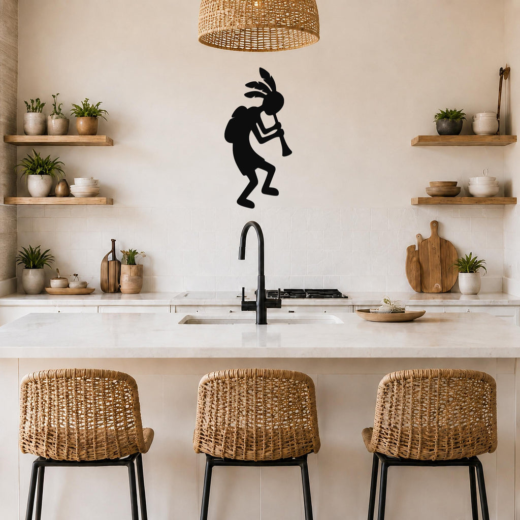 Black metal Kokopelli wall art silhouette playing a flute, mounted on a kitchen wall above a counter with open shelves and wicker bar stools.