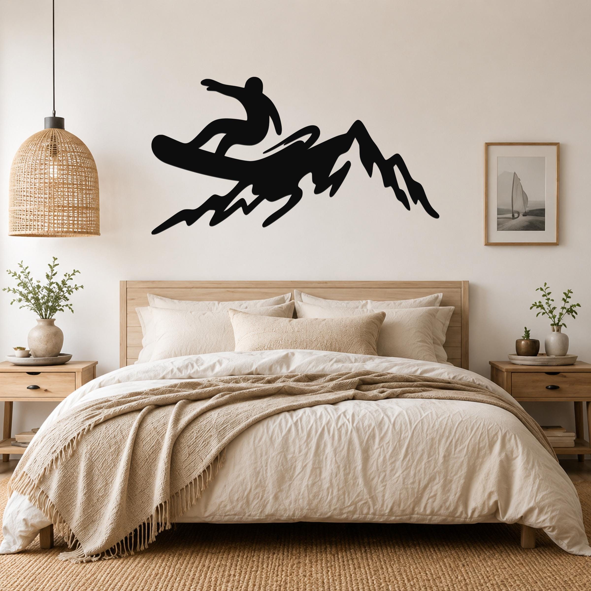 Black metal wall art silhouette of a snowboarder on a mountain, mounted above a bed in a bedroom.
