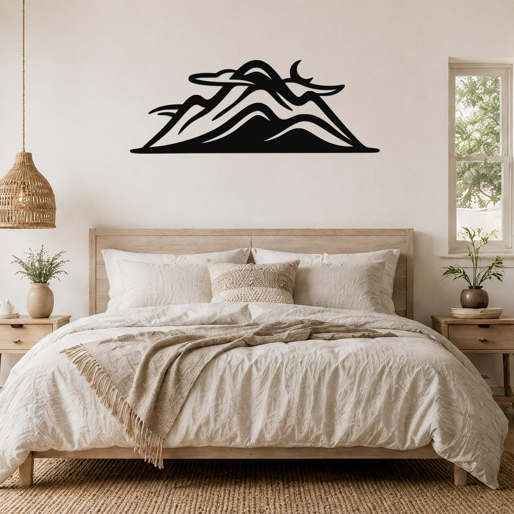 Black metal mountain silhouette wall art with layered peaks and a crescent moon cutout, mounted above a wooden bed in a neutral bedroom.