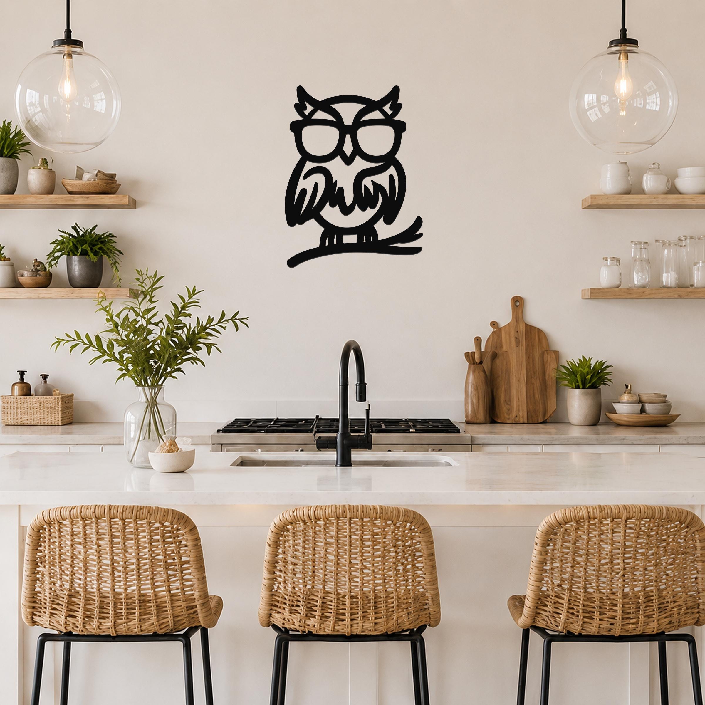Black metal owl wall art with glasses and a branch silhouette, mounted on a kitchen wall above a counter.
