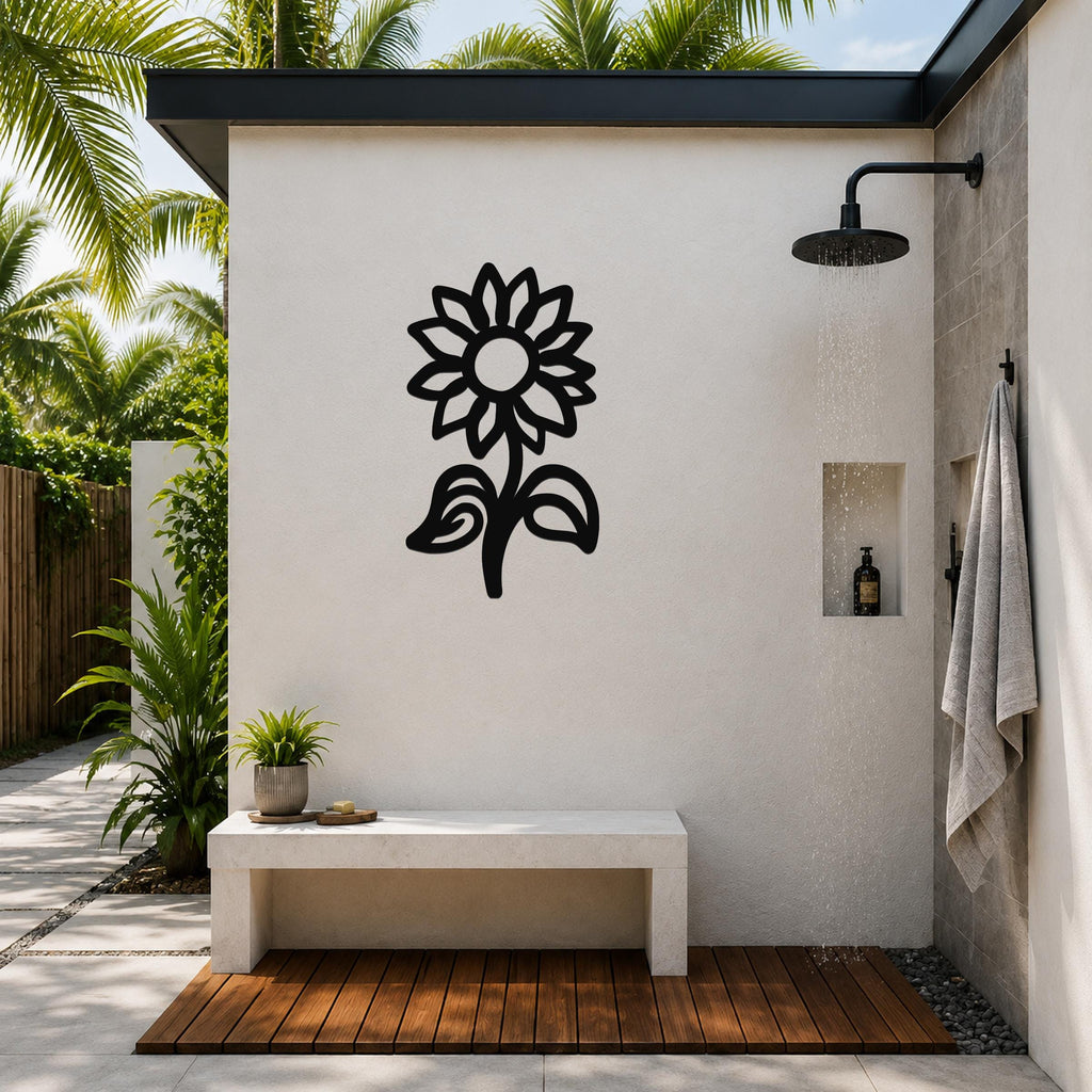 Black metal sunflower wall art with detailed petal and leaf cutouts, mounted on a white outdoor shower wall above a concrete bench.