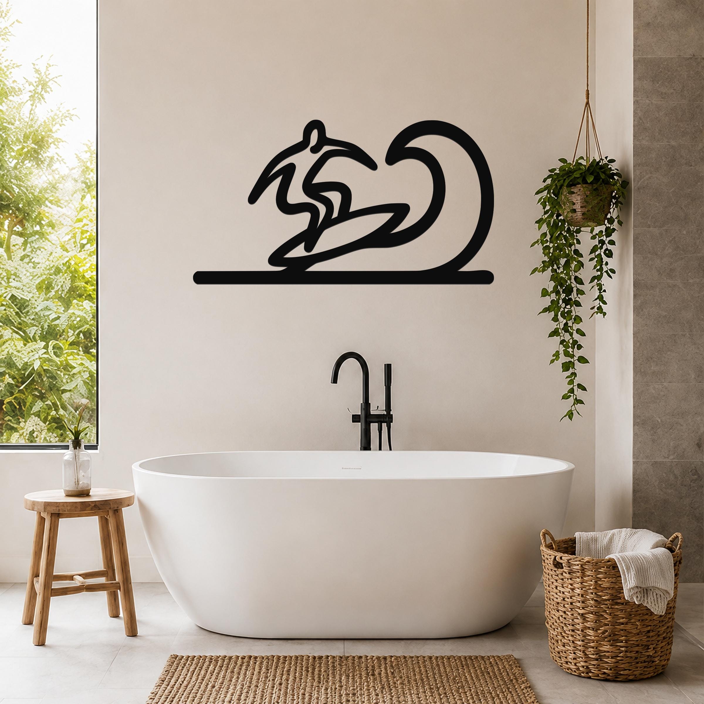 Black metal surfer wall art with wave silhouette, mounted above a freestanding bathtub in a modern bathroom.