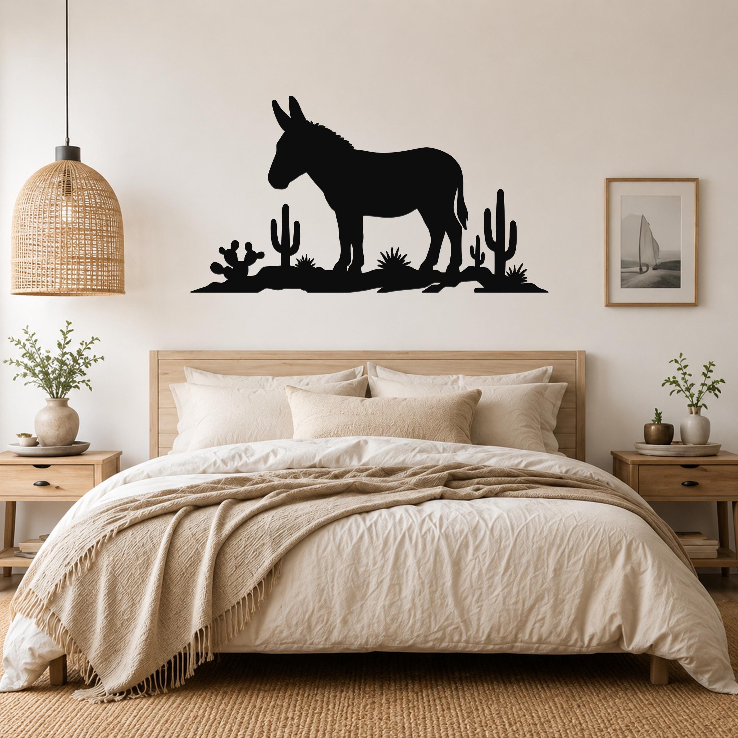 Black metal wall sculpture of a burro silhouette with cacti, mounted above a bed in a neutral bedroom.