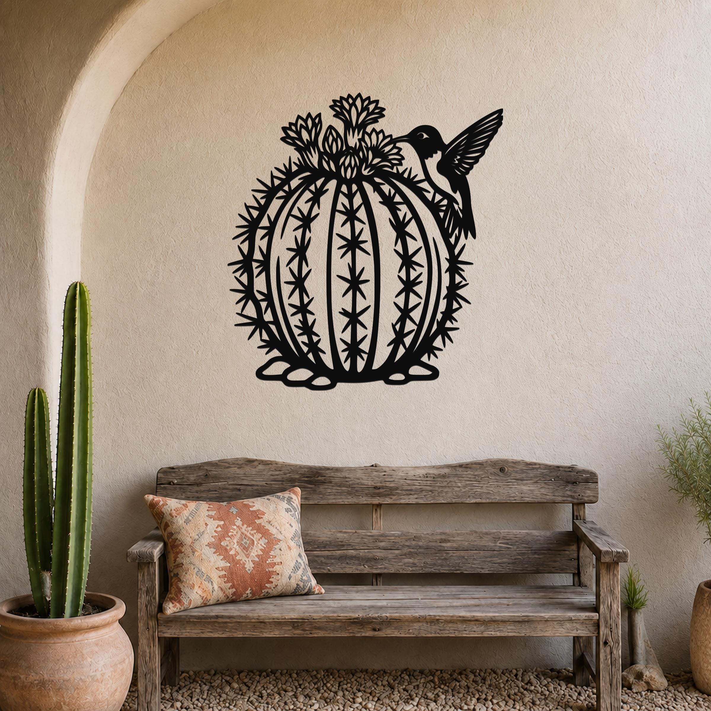Round black metal barrel cactus wall sculpture with flower and hummingbird cutouts, mounted on a textured wall above a wooden bench in a southwestern-style entryway.
