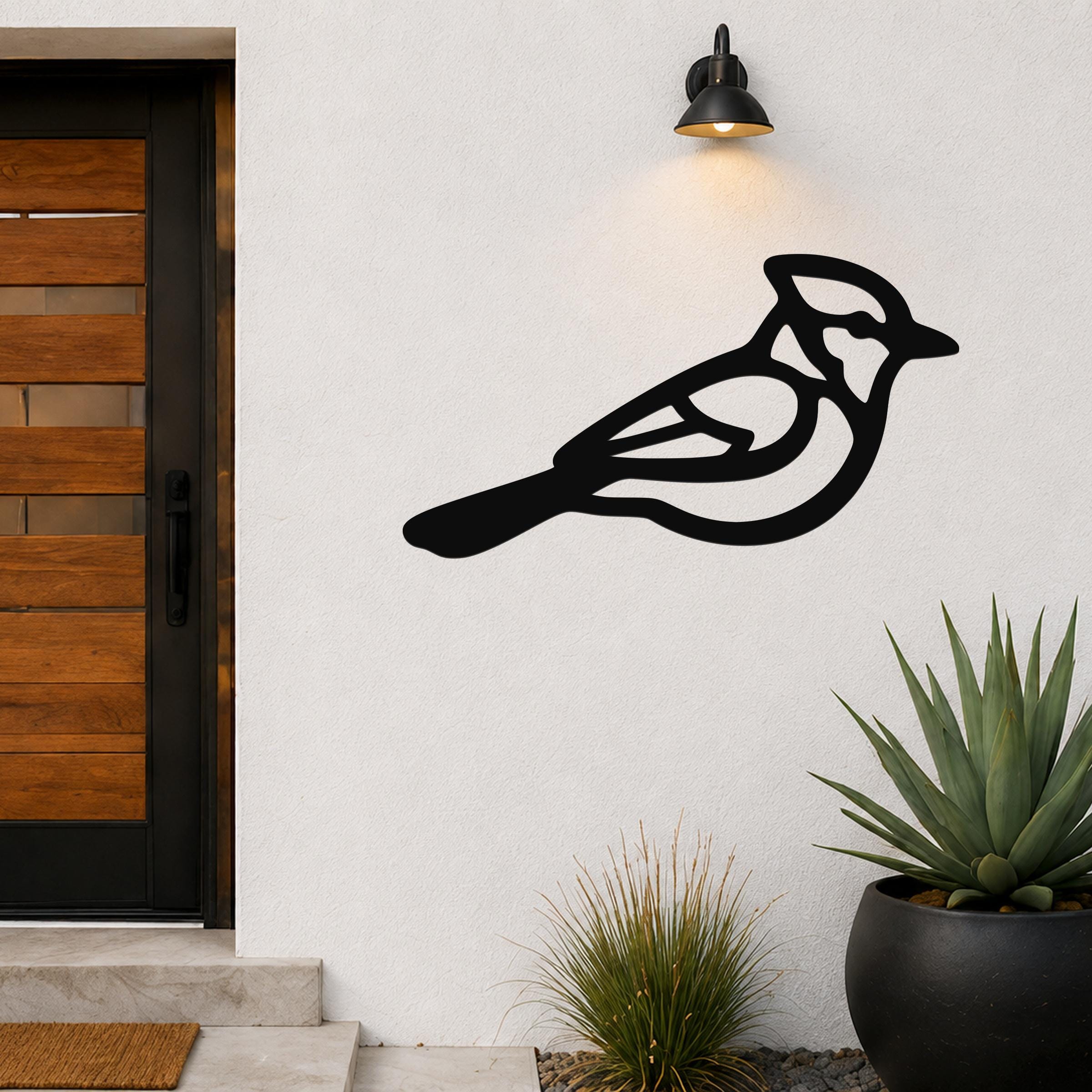 Black metal blue jay wall art with internal cutout details, mounted on an outdoor wall beside a wooden door and potted plants.