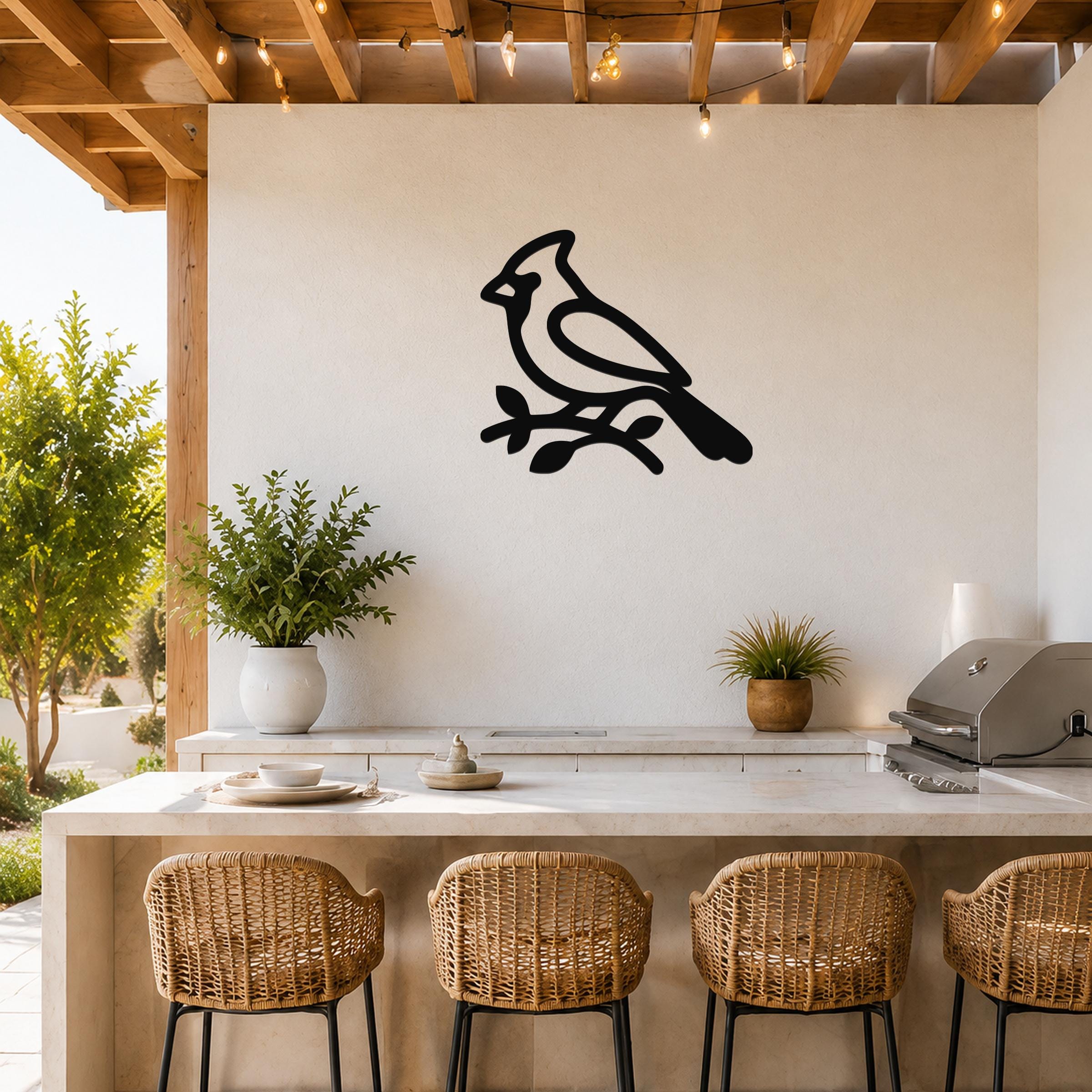 Black metal cardinal wall art silhouette perched on a branch, mounted on a white outdoor wall above a kitchen counter.