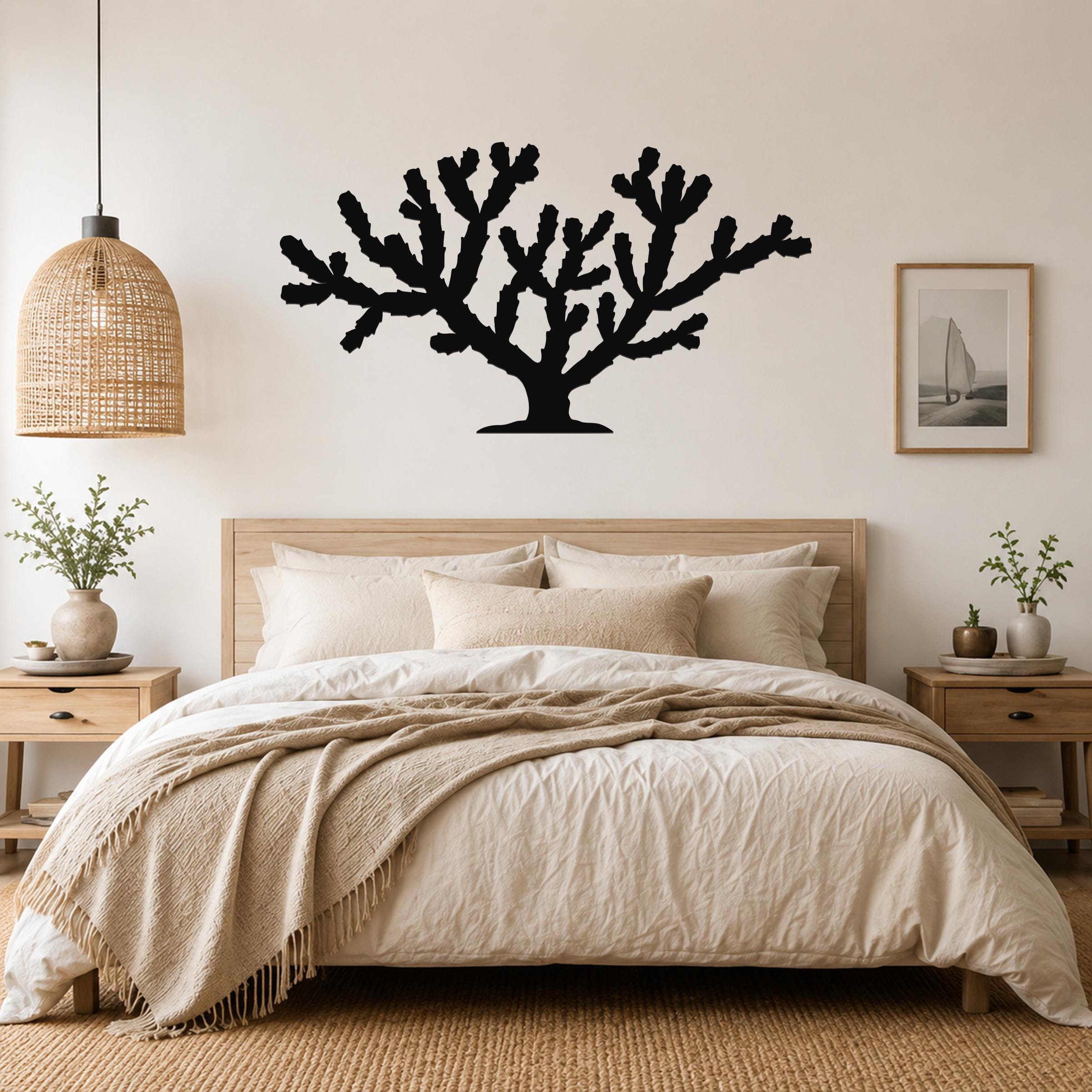 Black metal Cholla cactus wall art silhouette with branching arms, mounted above a bed in a neutral bedroom.