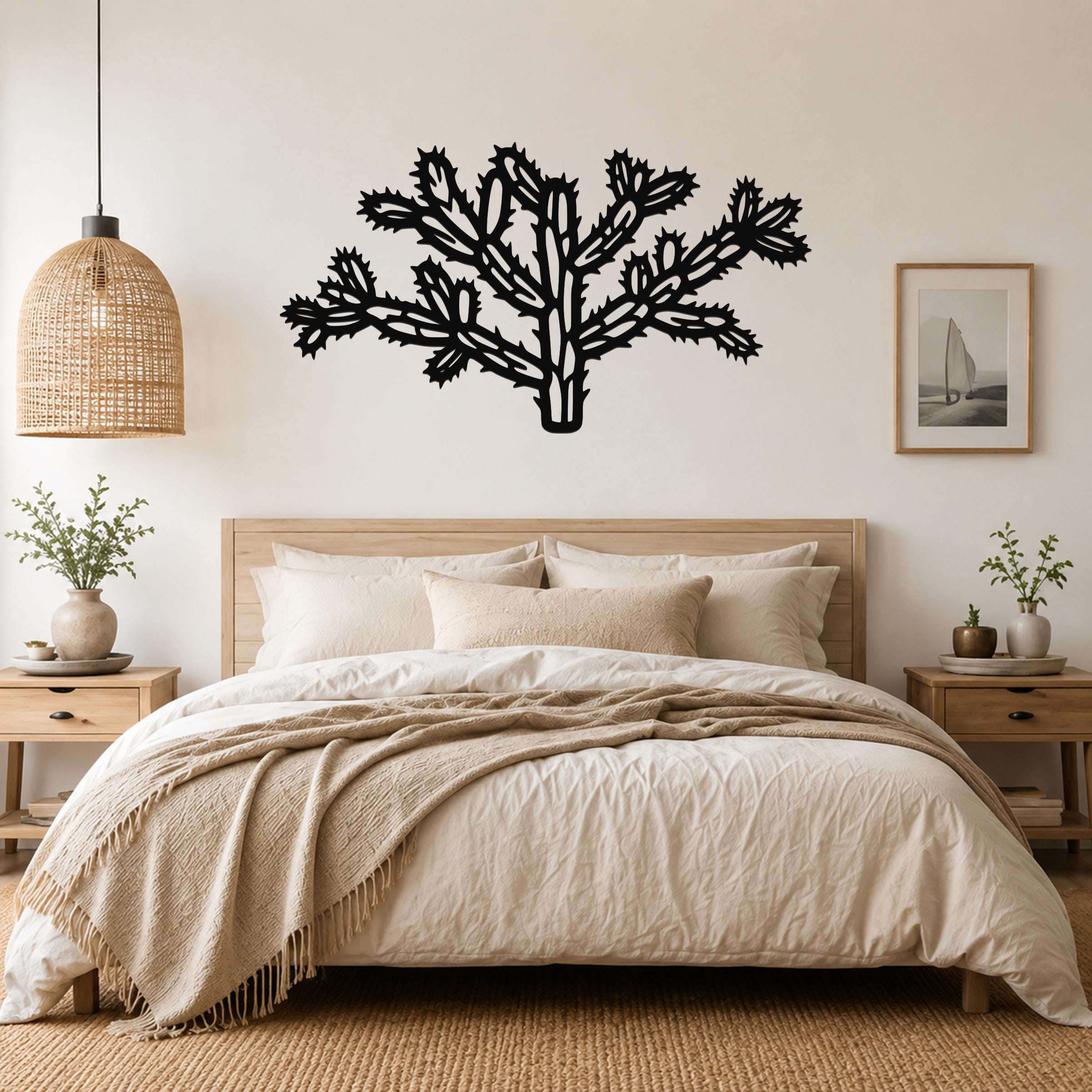 Black metal cholla cactus wall art with intricate branch and spine cutouts, mounted above a bed in a neutral bedroom.