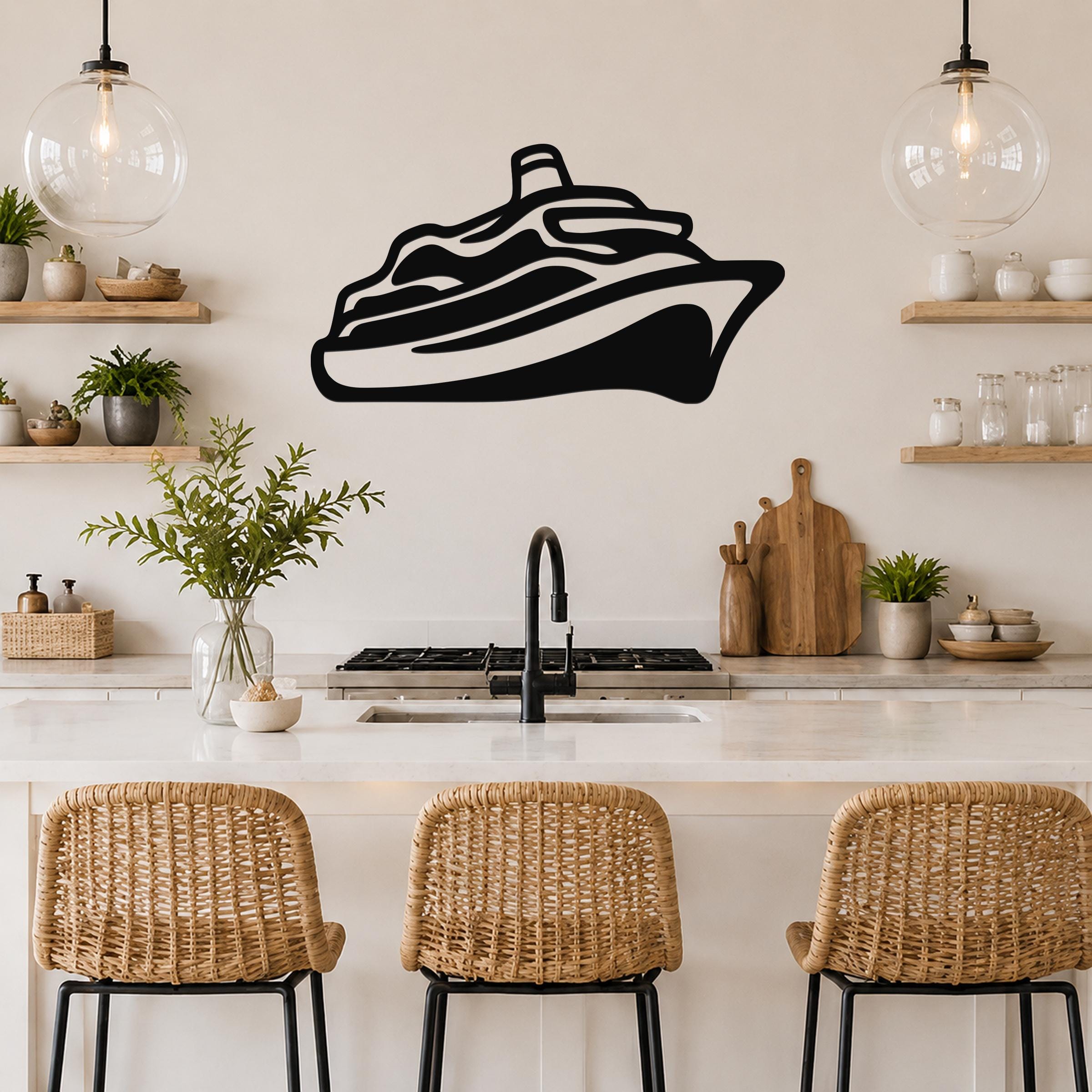 Black metal cruise ship wall art silhouette mounted above a kitchen counter, featuring a minimalist cutout design with visible deck layers and a smokestack, displayed in a modern kitchen with open shelving and pendant lights.