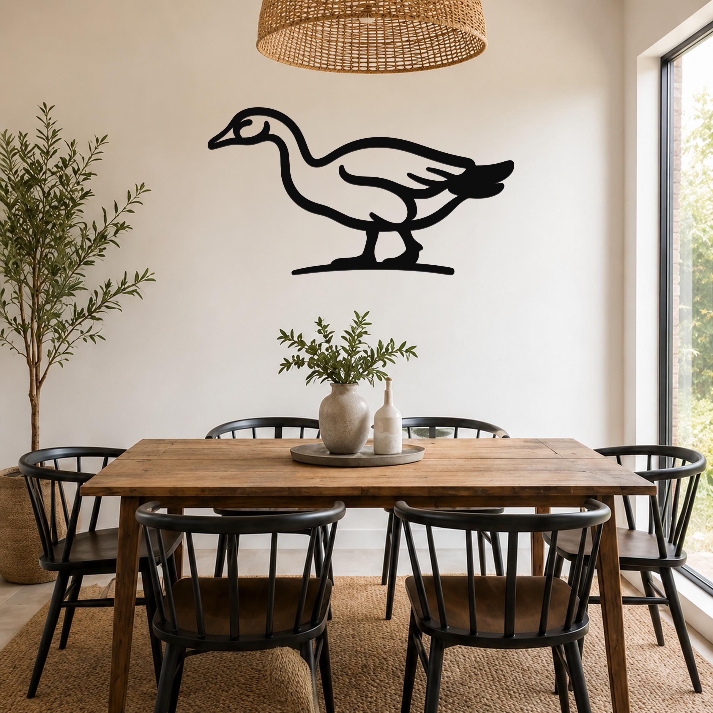Black metal goose wall art silhouette mounted on a white wall above a wooden dining table in a bright dining room.
