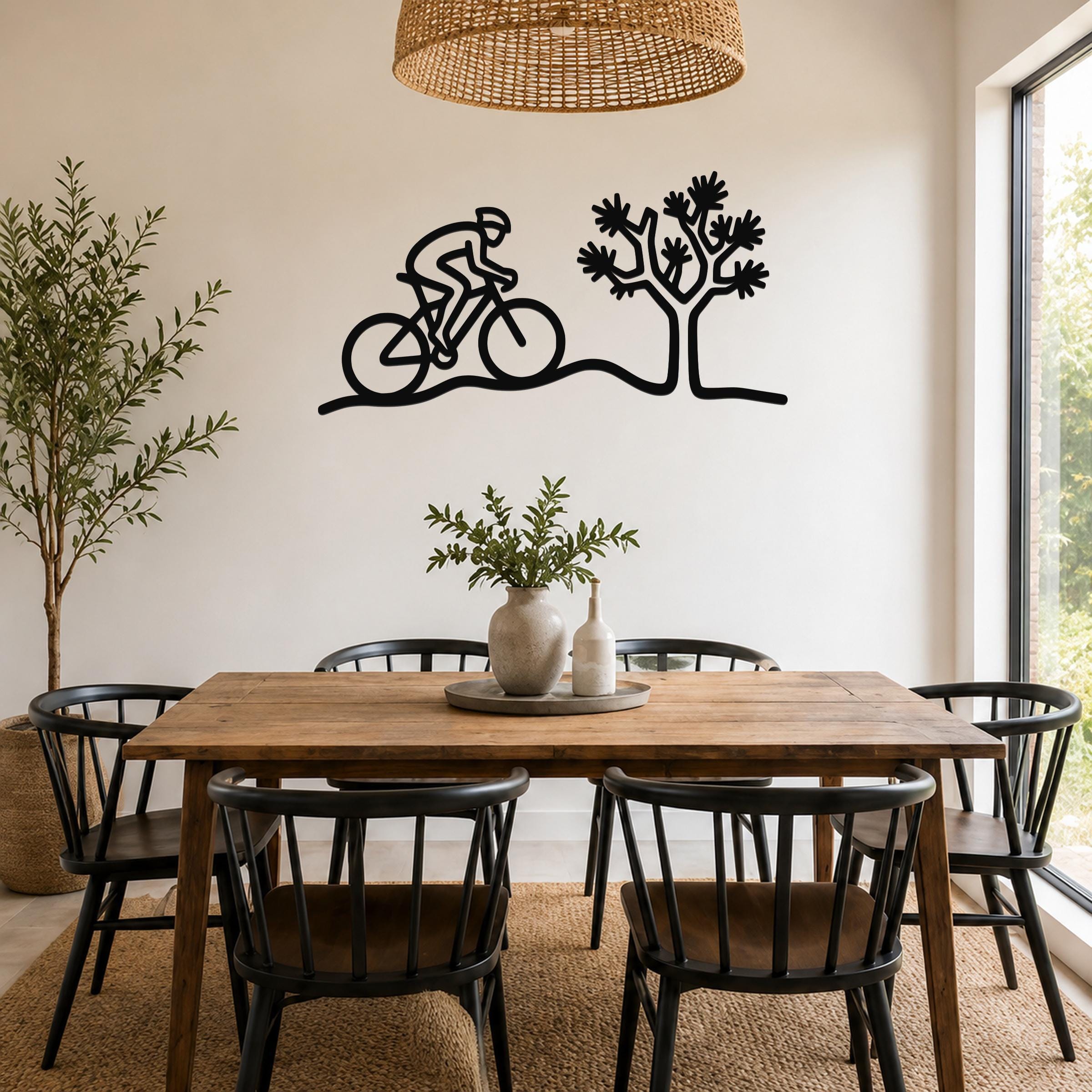 Black metal wall art silhouette of a cyclist and a Joshua tree, mounted on a dining room wall above a wooden table.