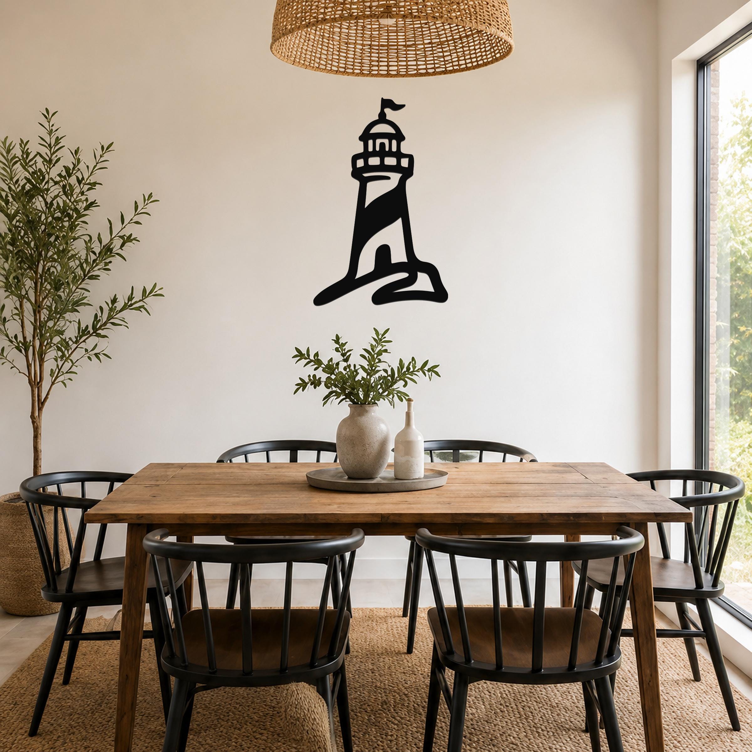 Black metal lighthouse wall art with a silhouette design, mounted on a white wall above a wooden dining table in a bright room.