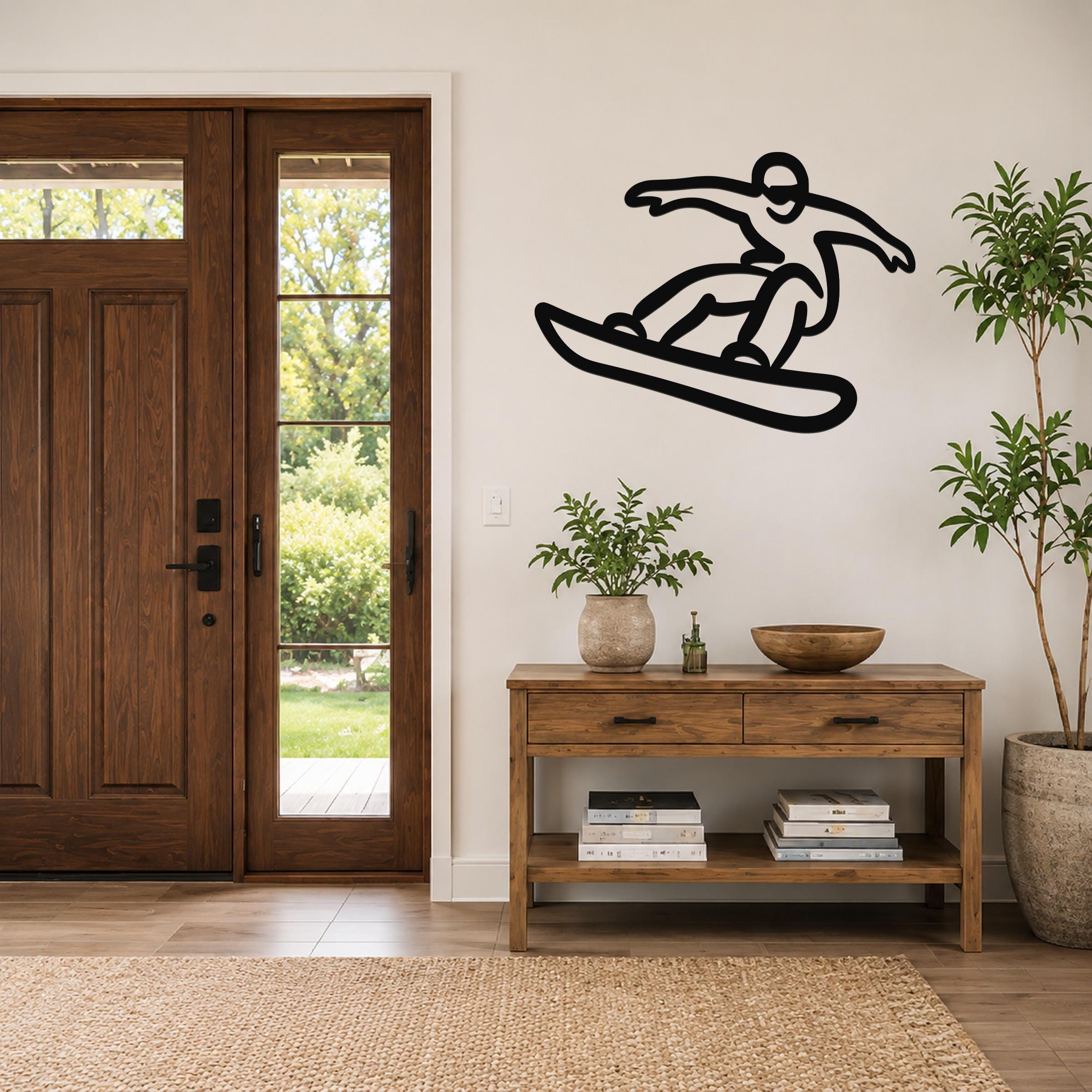 Black metal wall art silhouette of a snowboarder in motion, mounted on a wall above a wooden console table in a living room.