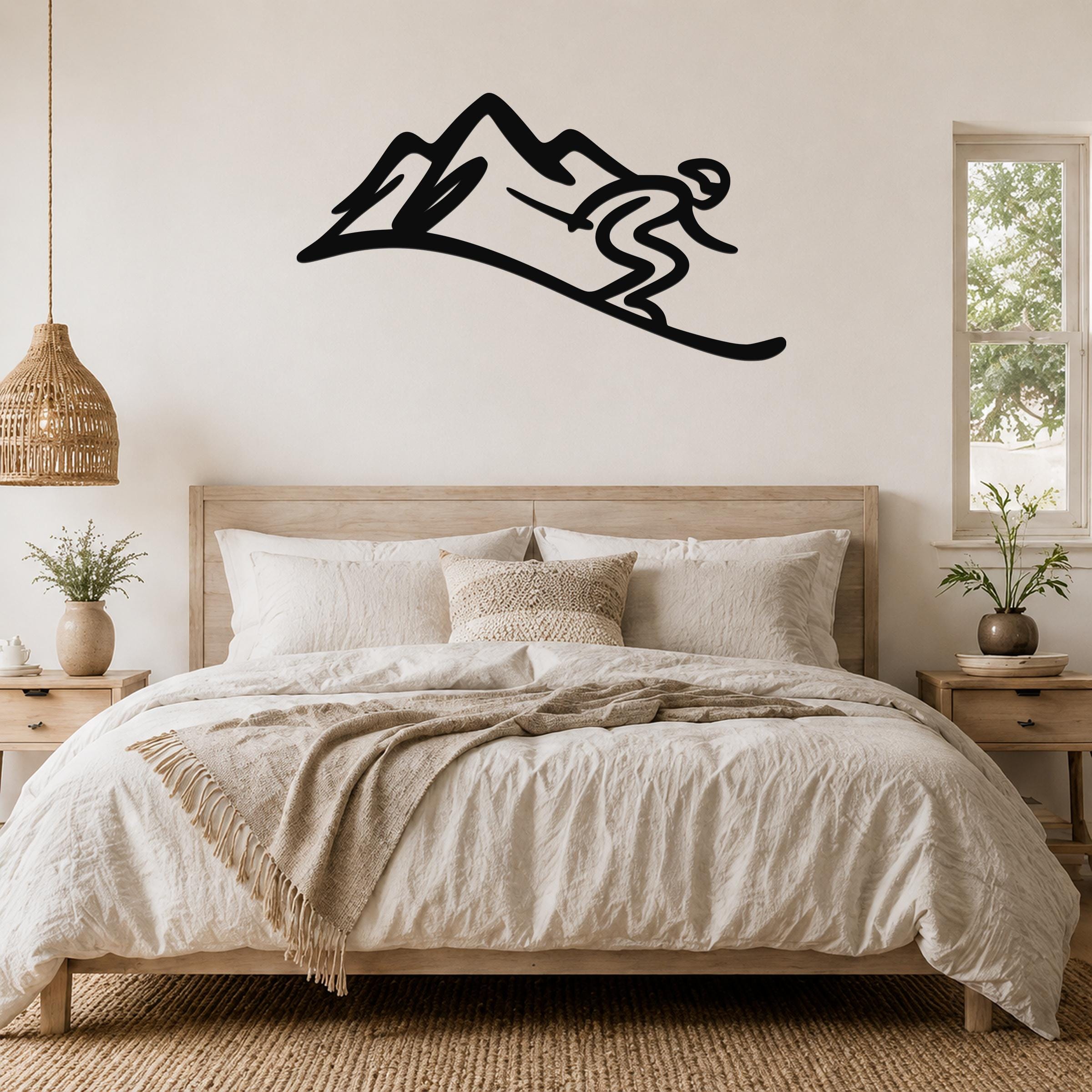 Black metal wall art featuring a skier silhouette on a mountain, mounted above a bed in a bedroom.
