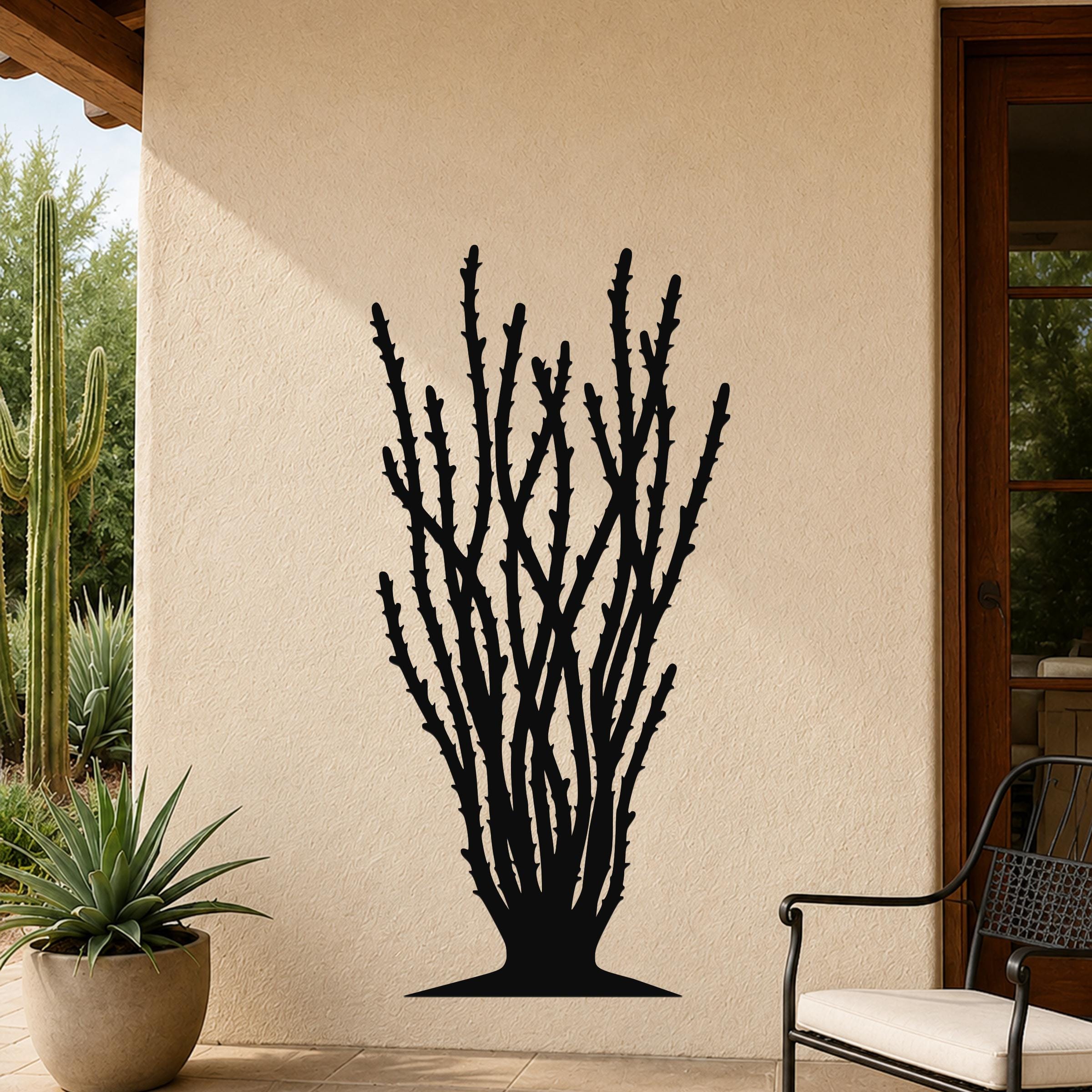 Black metal ocotillo wall art with spiny branch cutouts, mounted on a beige outdoor wall beside a patio chair and potted plant.