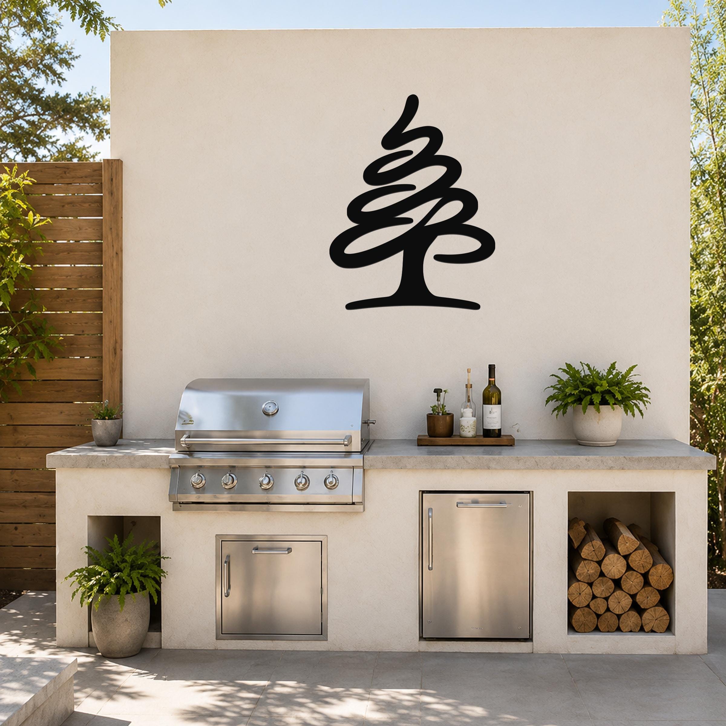 Black metal pine tree wall art silhouette mounted on a light-colored outdoor wall above a kitchen counter with a grill and storage.