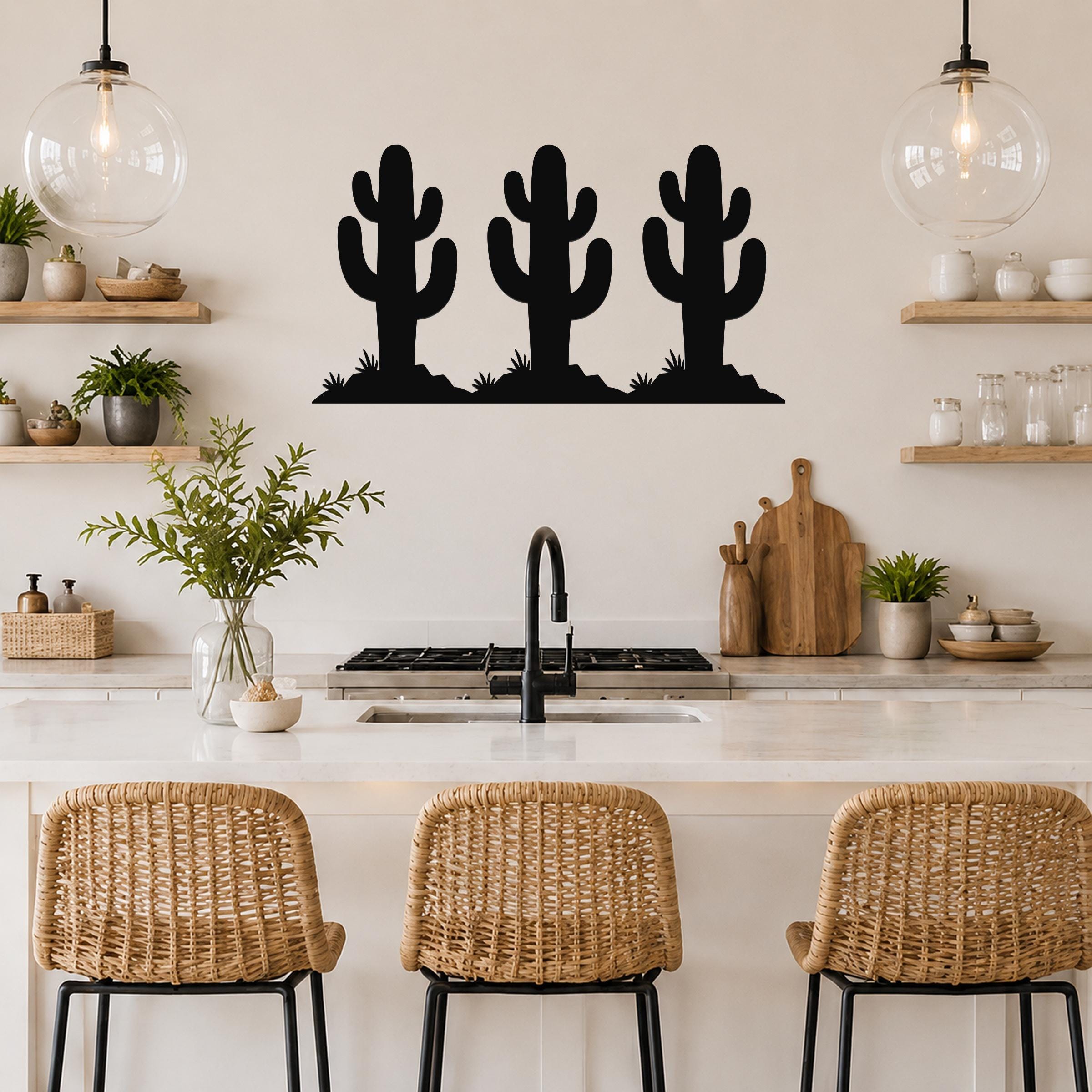 Black metal wall art featuring a trio of saguaro cactus silhouettes with spines and base grass, mounted above a kitchen counter.