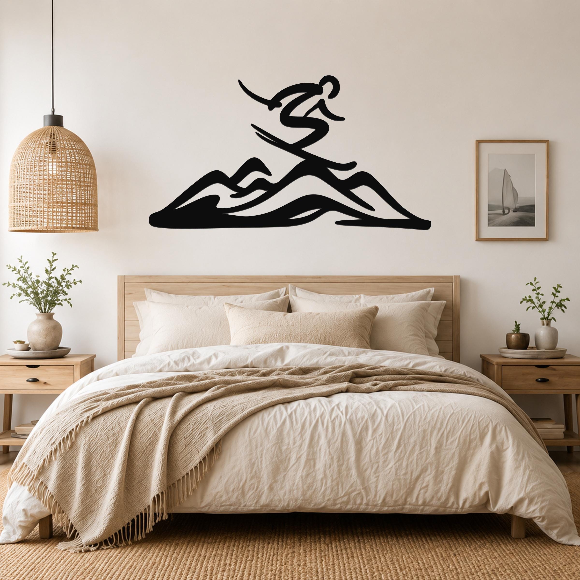 Black metal wall art featuring a skier silhouette above mountain peaks, mounted above a bed in a neutral bedroom.