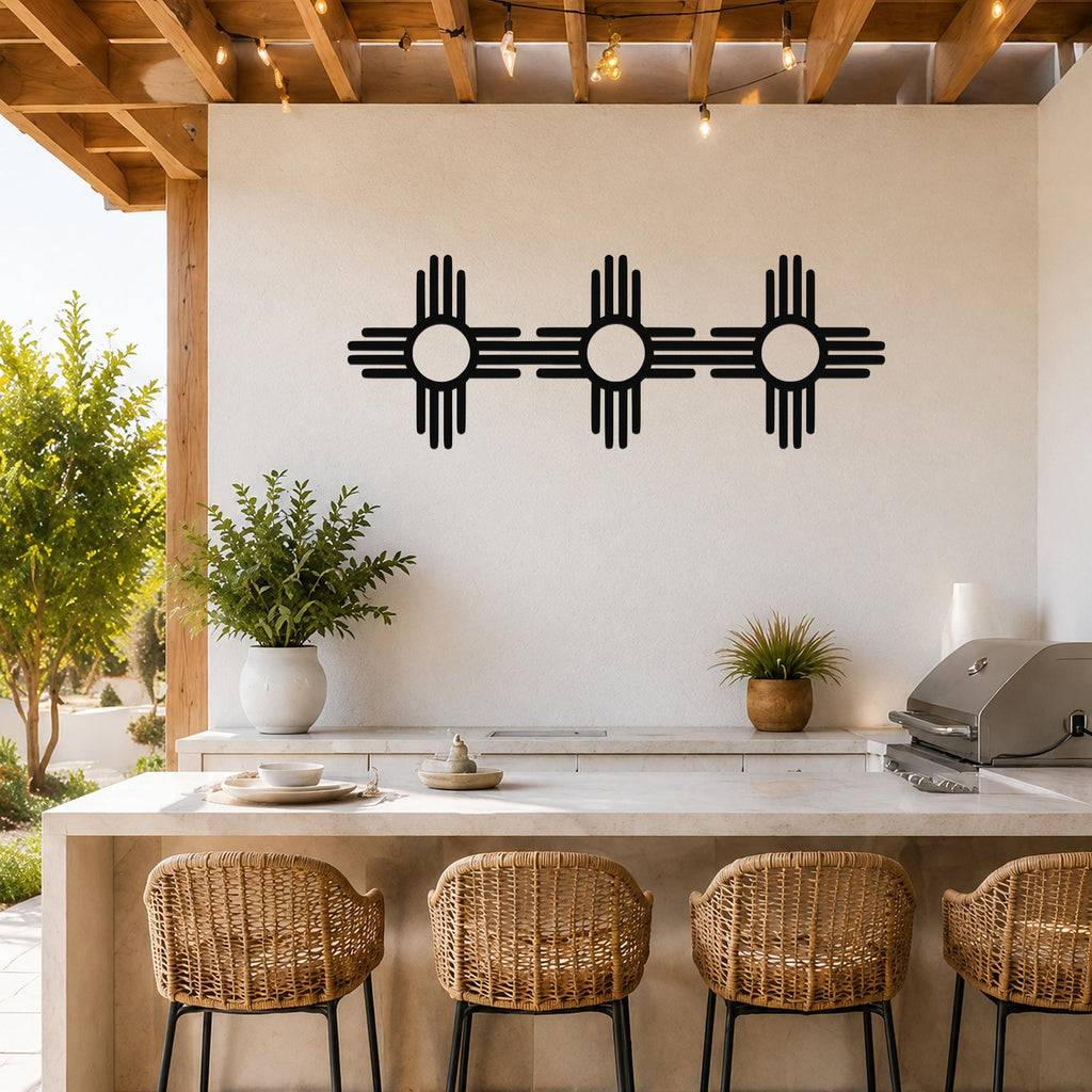 Black metal Zia Sun symbol trio wall art with four rays on each of three connected suns, mounted on a white wall above a kitchen counter on a covered patio.