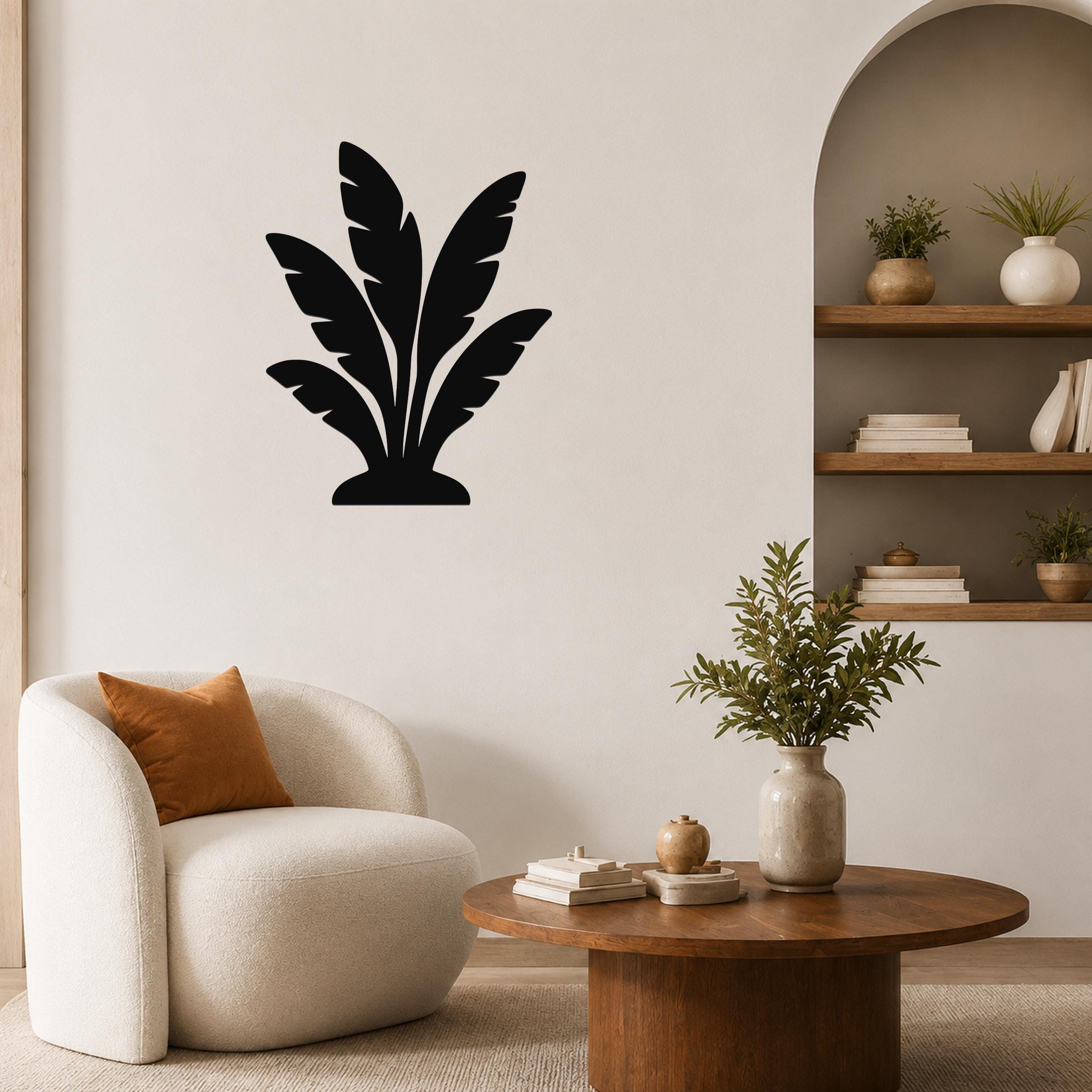Black metal wall art in a tropical leaf silhouette design, mounted on a living room wall above a white armchair.