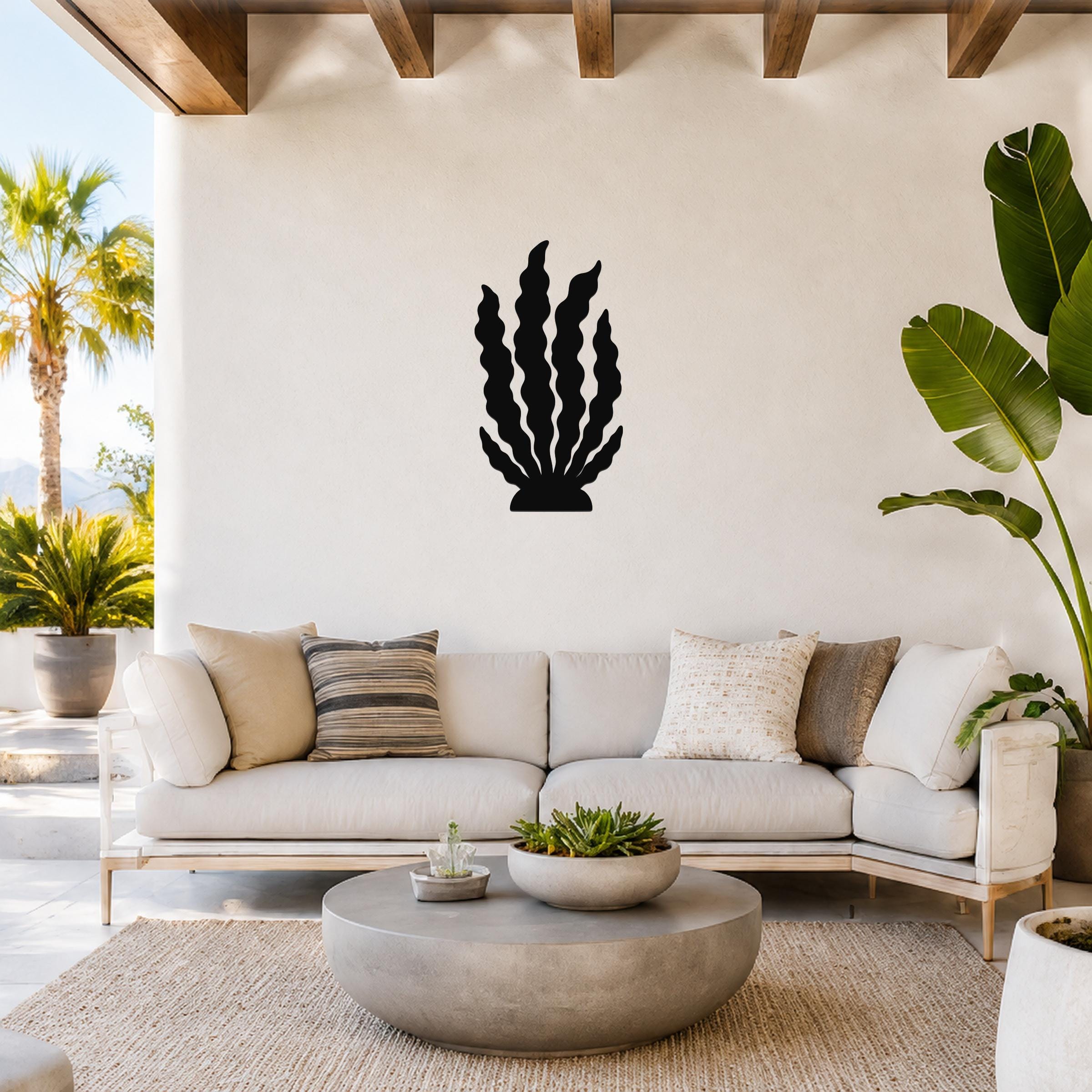 Black metal kelp wall art with wavy leaf cutouts, mounted on a white wall above a light-colored sofa in a bright living room.