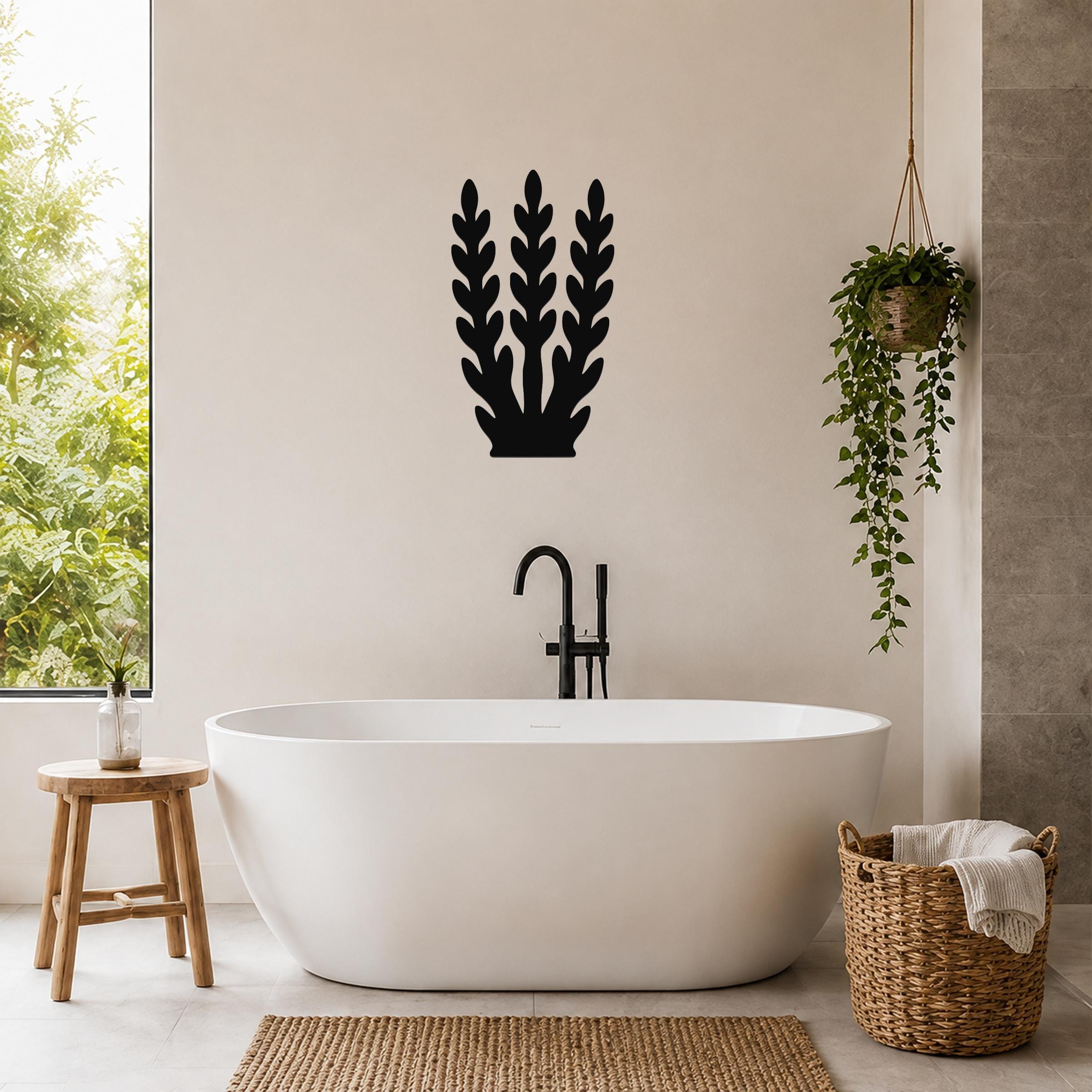 Black metal kelp wall art with layered leaf cutouts, mounted on a bathroom wall above a freestanding tub.