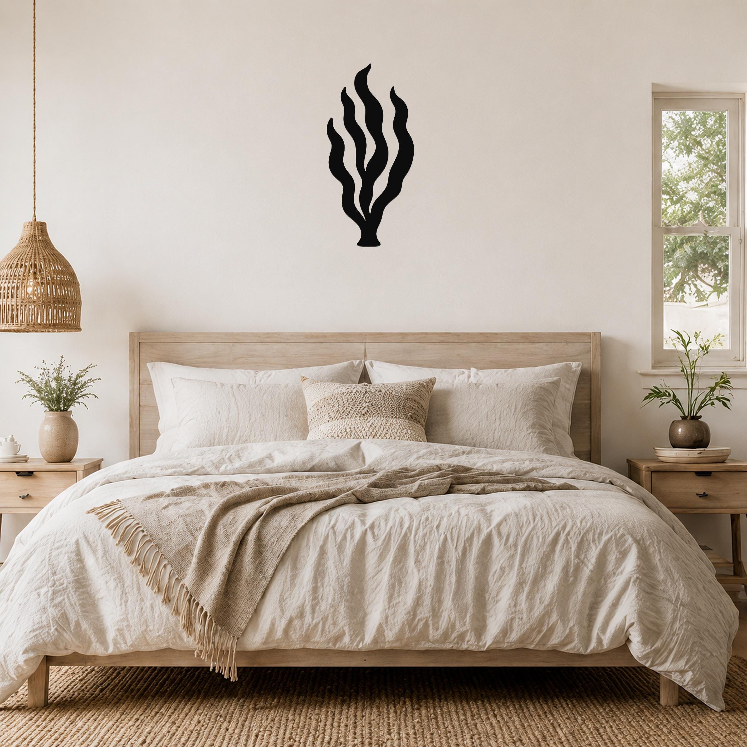 Black metal kelp seaweed wall art with flowing frond cutouts, mounted above a wooden bed in a coastal-style bedroom.