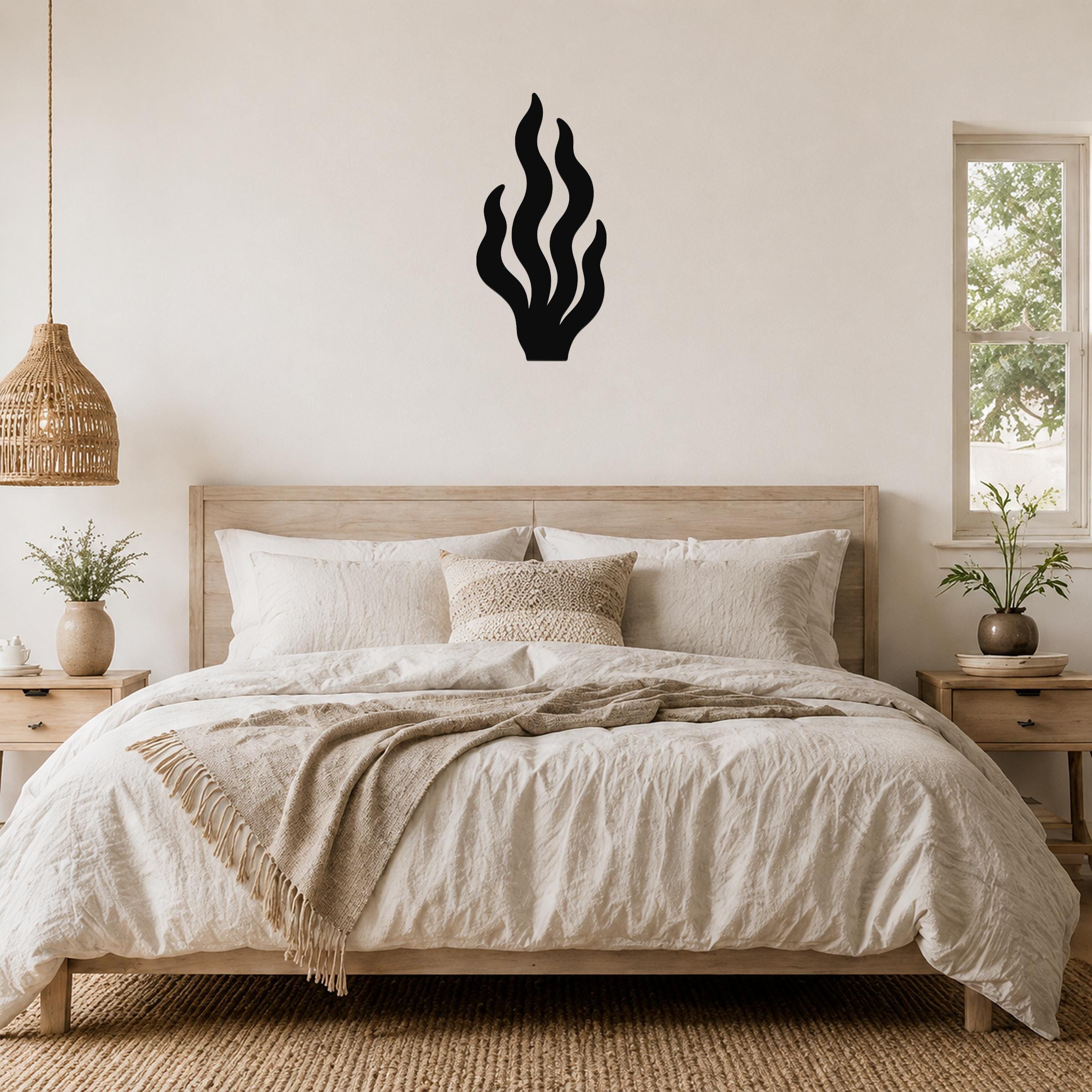 Black metal kelp wall art with flowing frond cutouts, mounted above a wooden bed in a neutral bedroom.