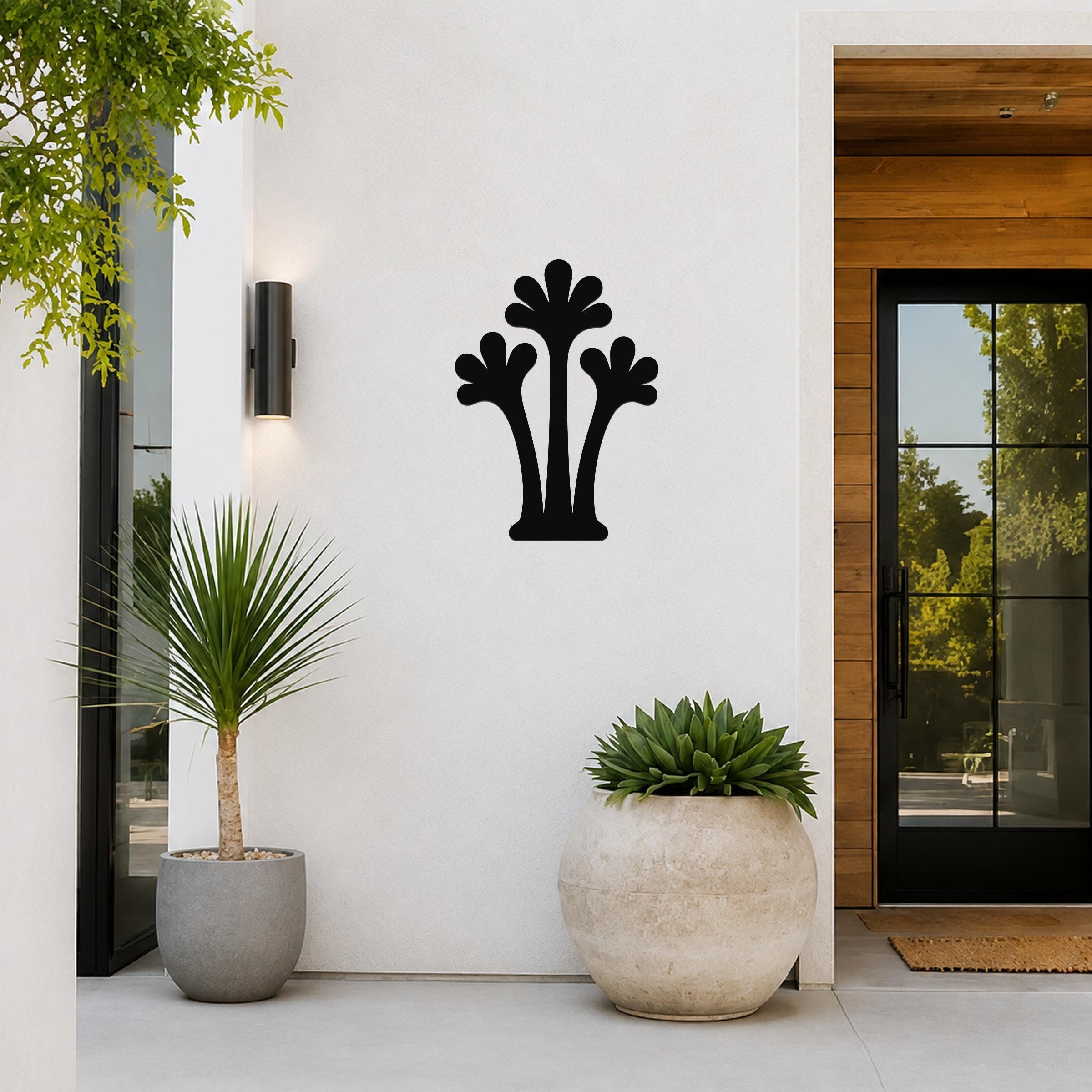 Black metal palm tree wall art with three fronded silhouettes, mounted on a white exterior wall beside a glass door and potted plants.