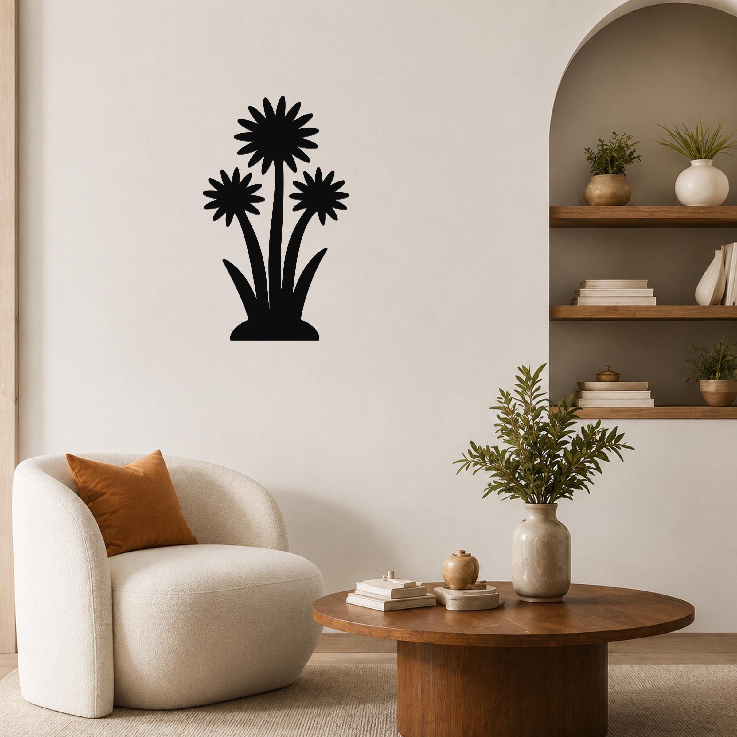 Black metal wall art featuring a silhouette of three wildflowers with layered petals and long stems, mounted on a living room wall above a round wooden coffee table.