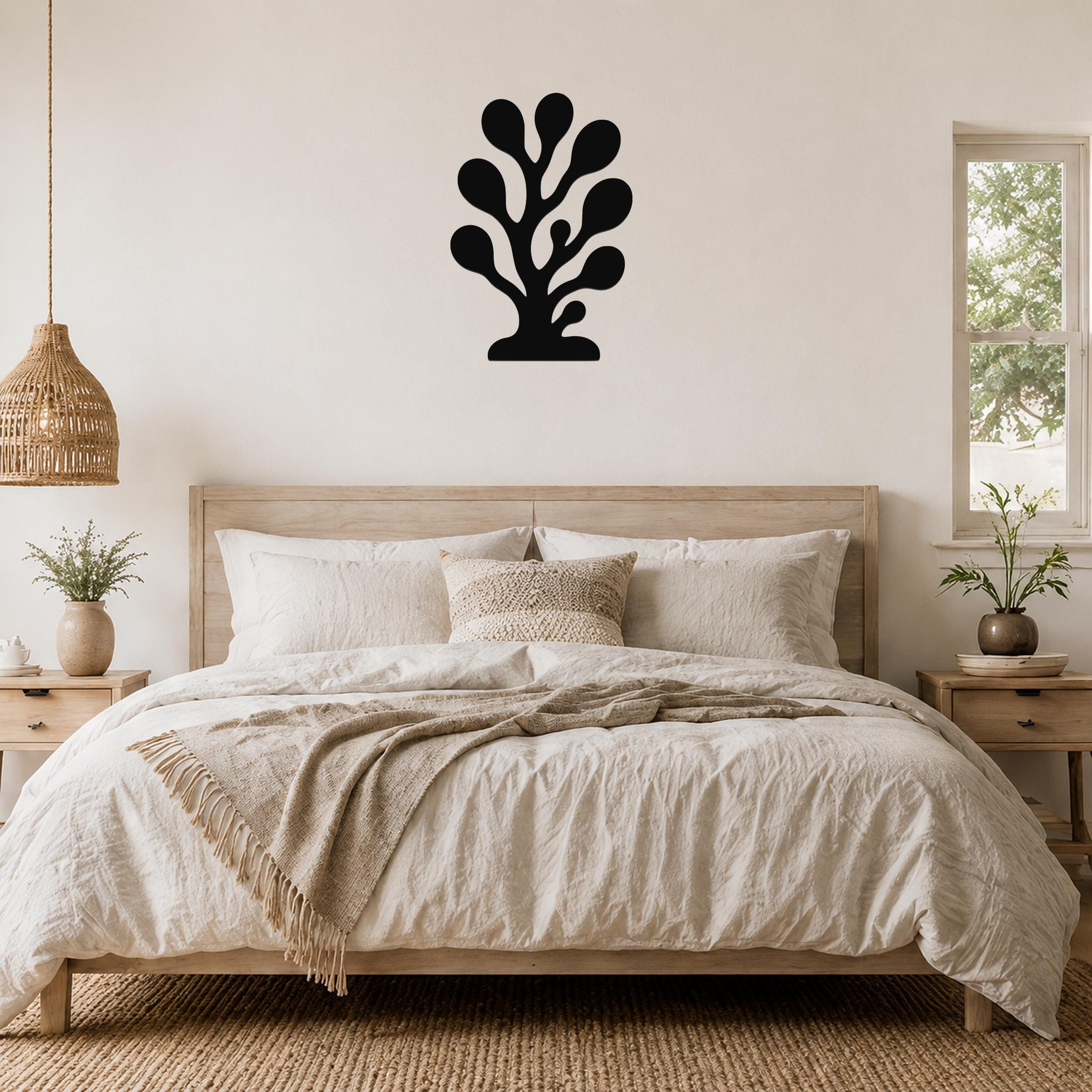 Black metal coral wall art with branching cutouts, mounted above a wooden bed in a neutral bedroom.