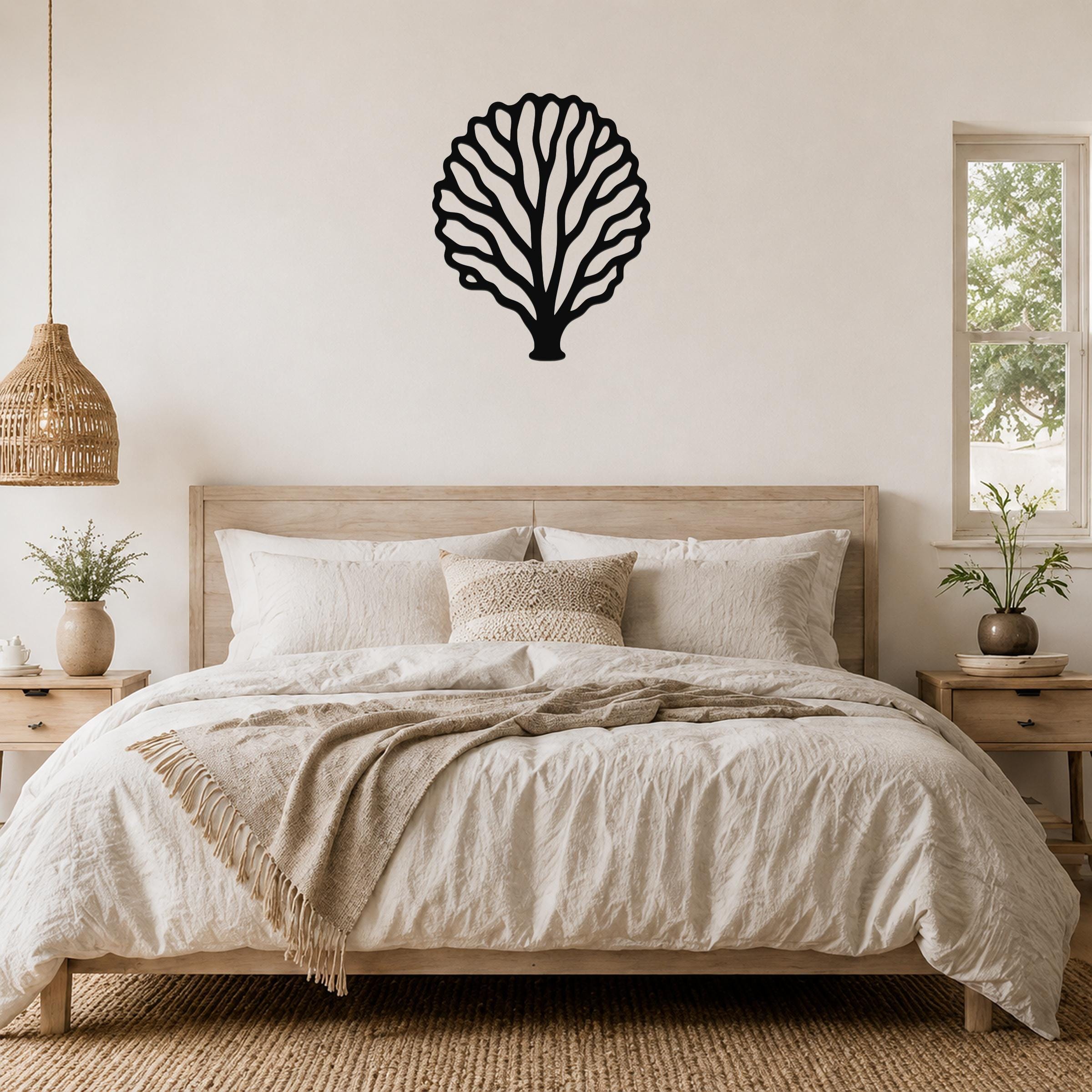 Black metal fan coral wall art with intricate branching cutouts, mounted above a wooden bed in a neutral bedroom.