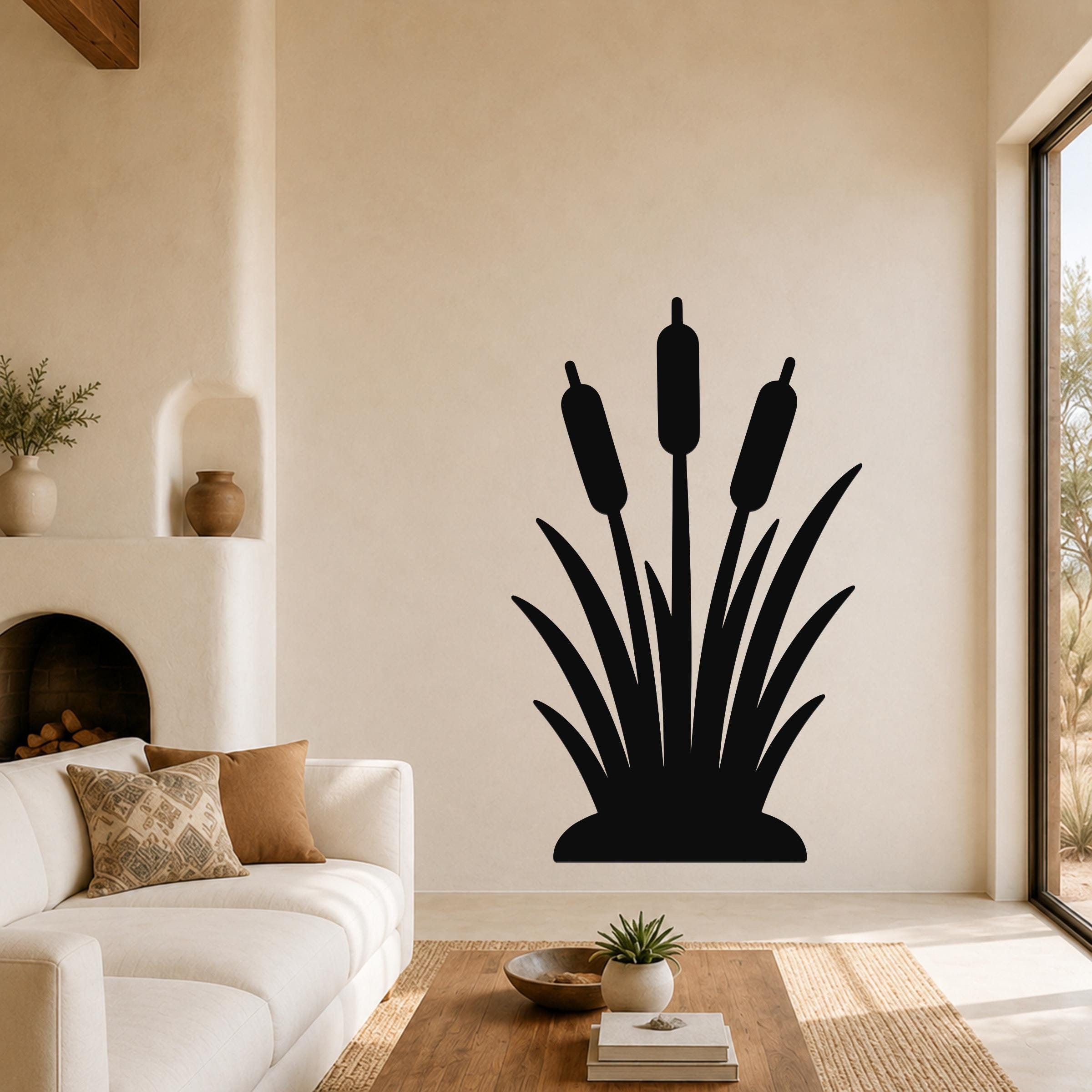 Black metal cattail wall art silhouette with three seed heads and leafy base, mounted on a living room wall above a white sofa.