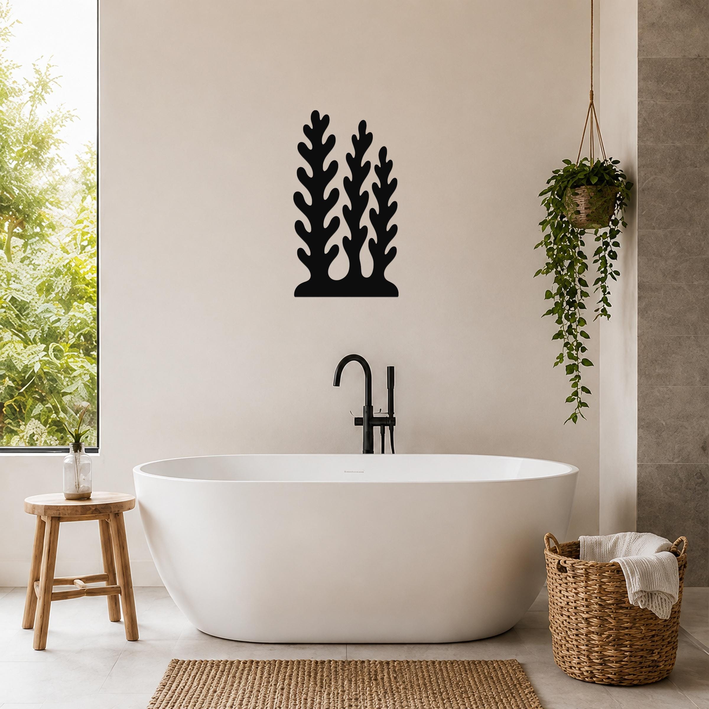 Black metal wall art with a kelp and seaweed silhouette design, mounted on a bathroom wall above a freestanding tub.