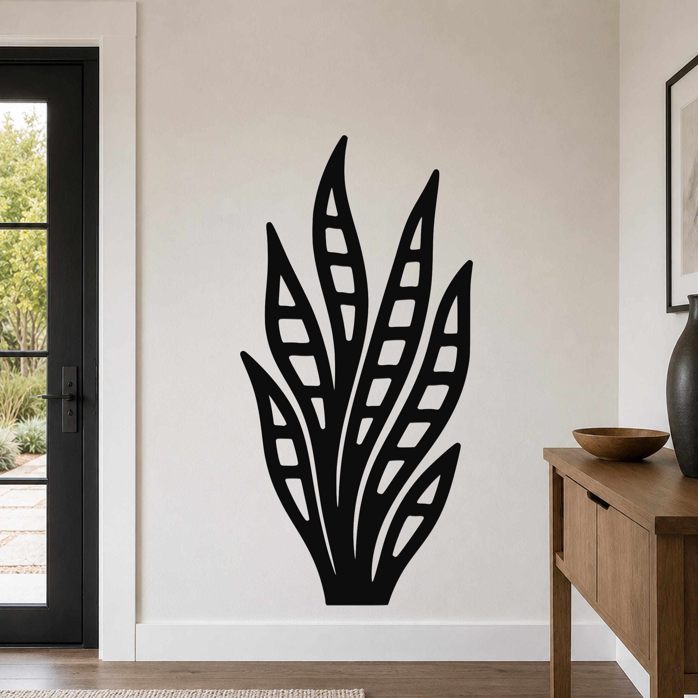 Black metal wall art in a snake plant silhouette with internal leaf cutouts, mounted on a living room wall above a wooden console table.
