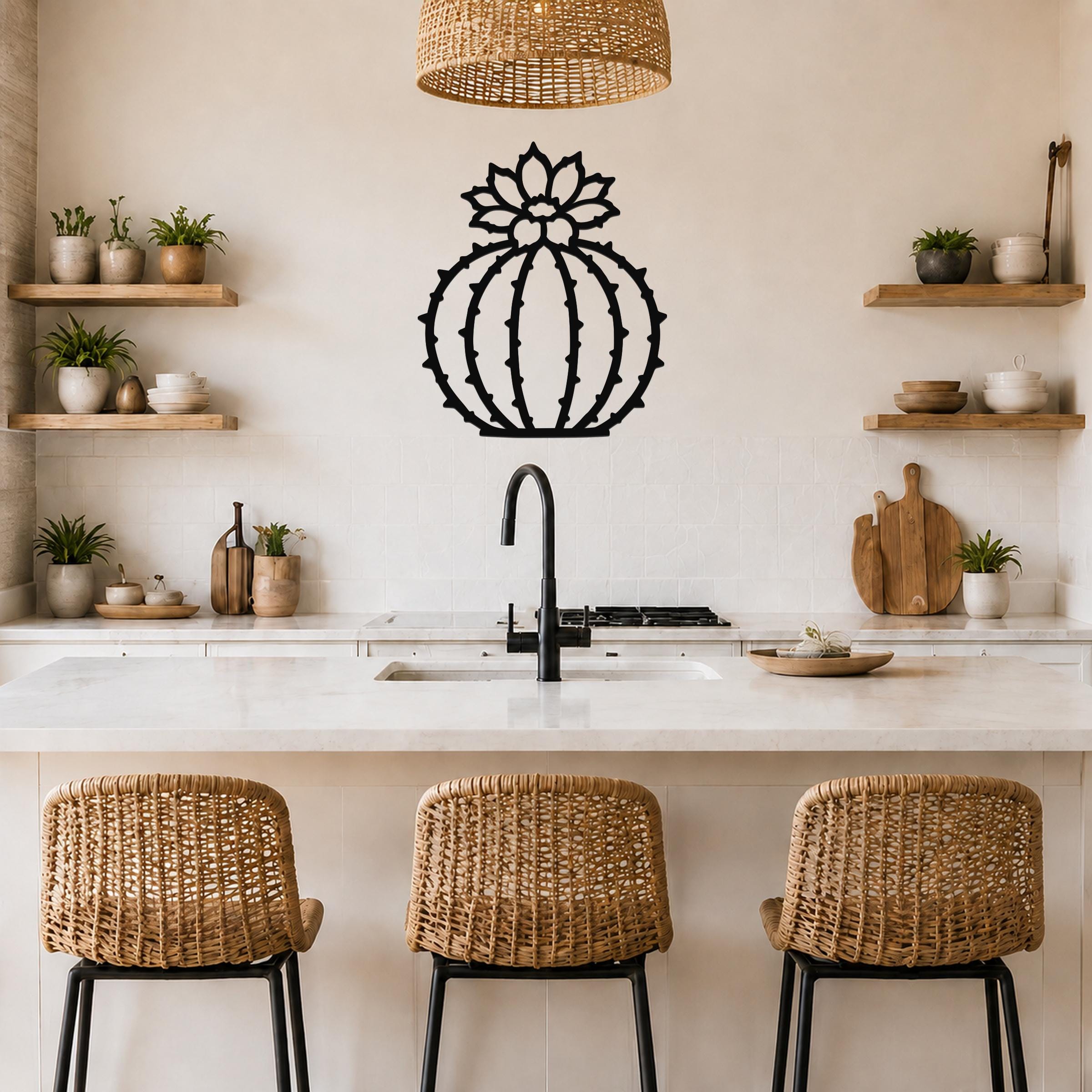 Black metal barrel cactus wall art with flower and spine cutouts, mounted on a kitchen wall above a counter.