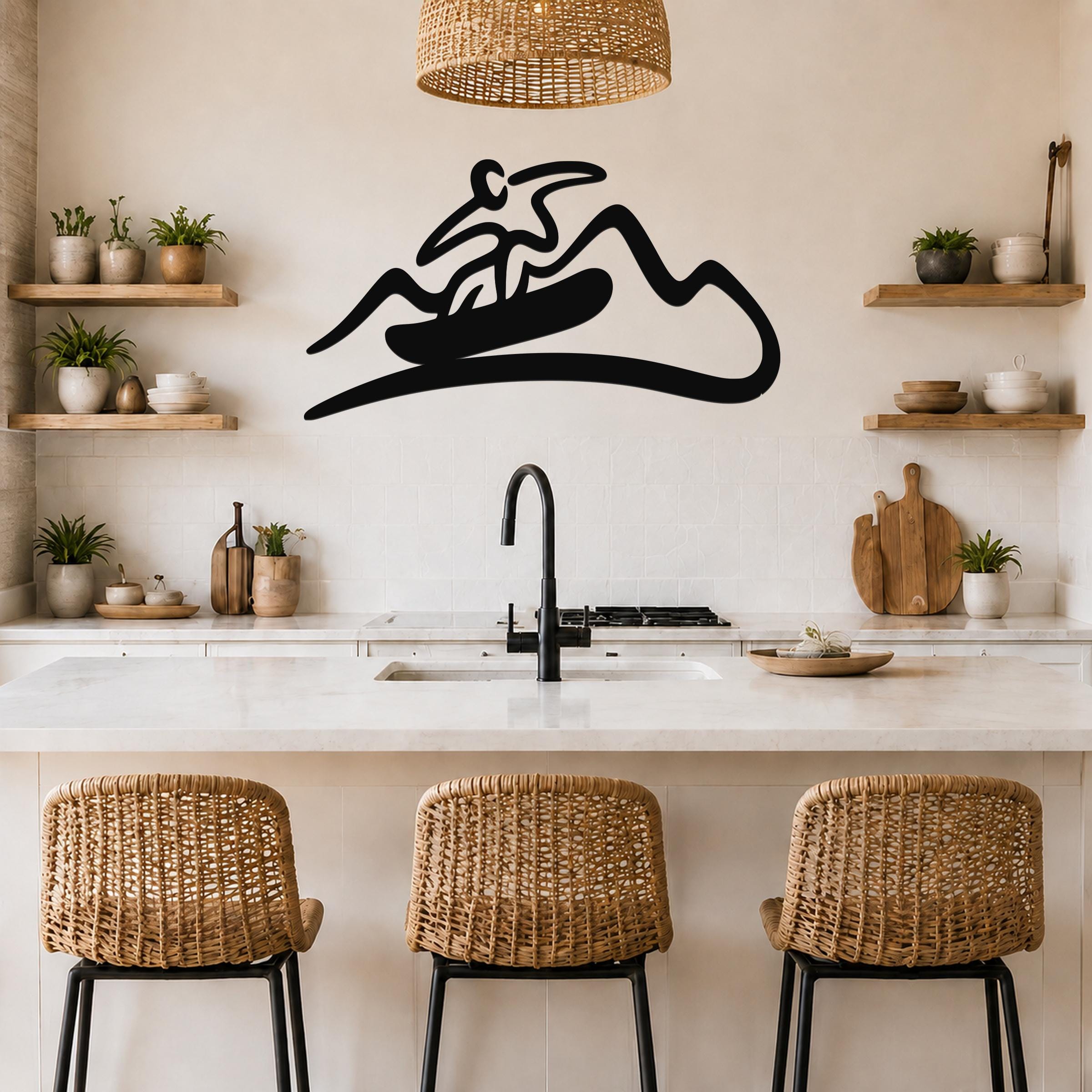 Black metal wall art silhouette of a snowboarder on a mountain, mounted above a kitchen counter with wicker stools and wooden shelves.