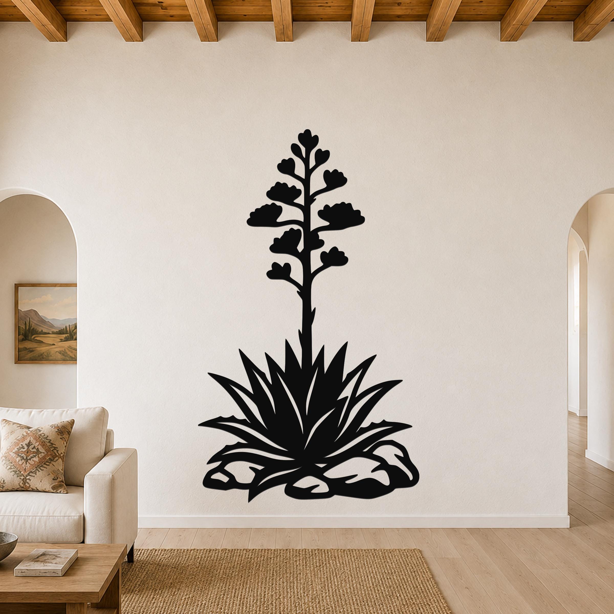 Black metal agave wall art with a tall flowering stalk and spiky rosette cutout, mounted on a living room wall above a sofa.