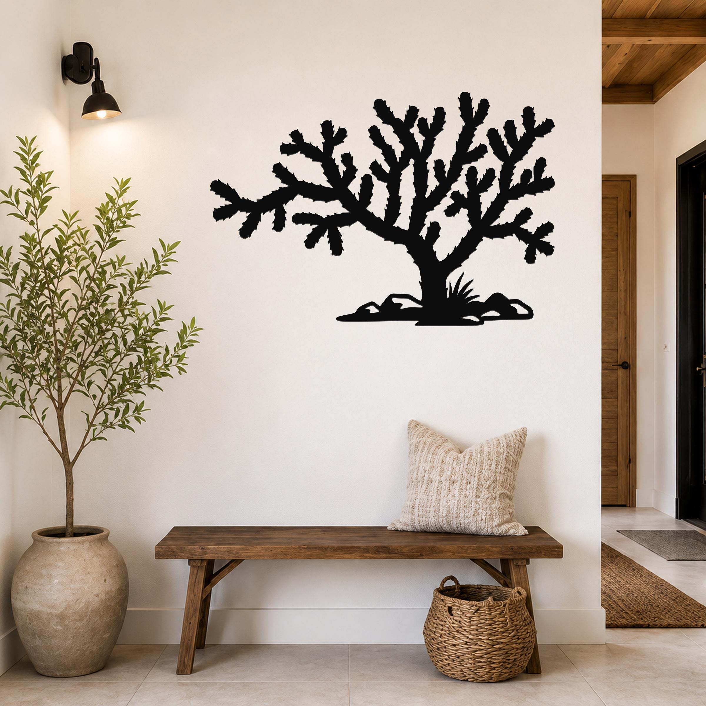 Black metal Cholla cactus wall art silhouette with branching arms and base cutouts, mounted on a white wall above a wooden bench in a hallway.