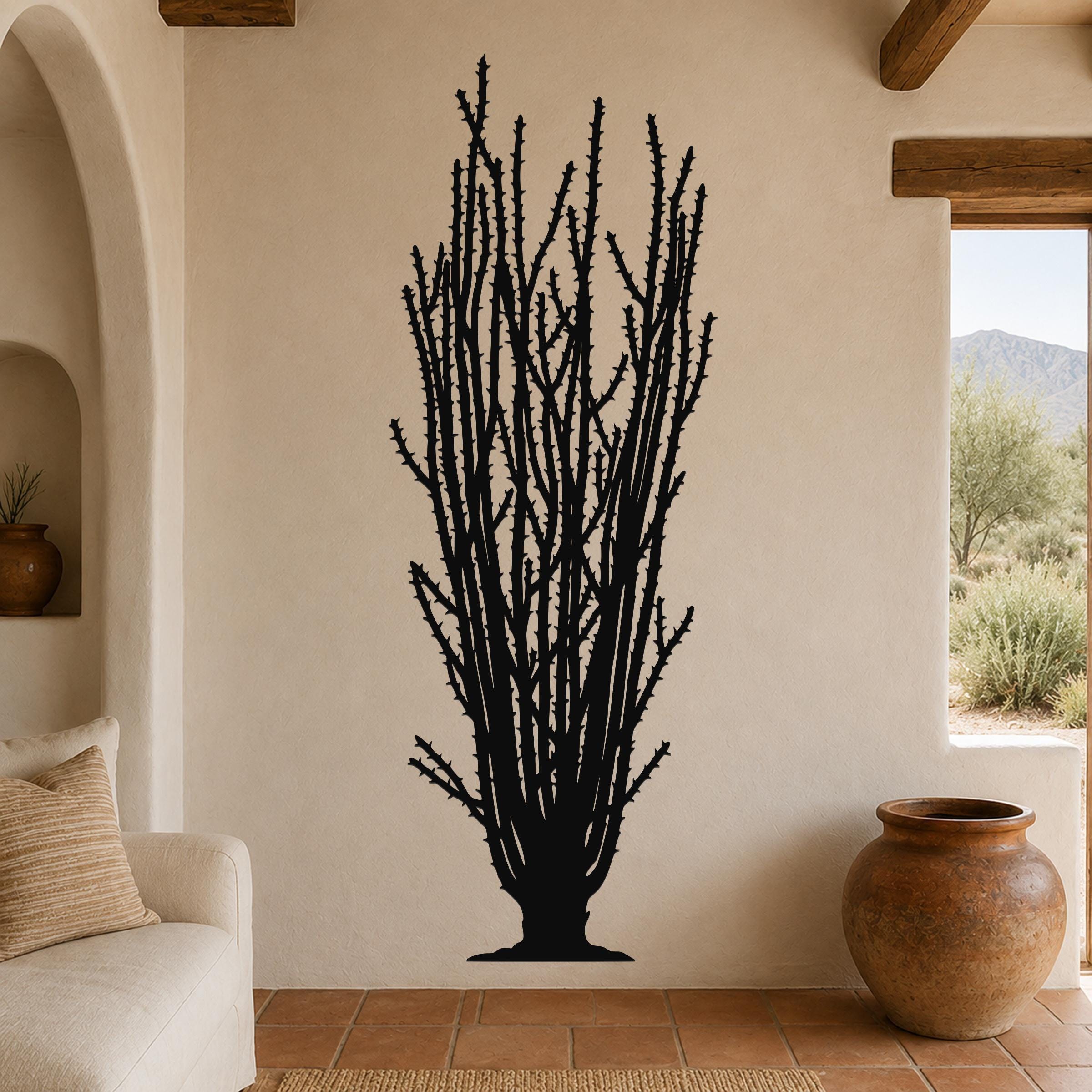 Black metal wall art silhouette of a tall ocotillo cactus with spiny branches, mounted on a beige living room wall above a sofa.