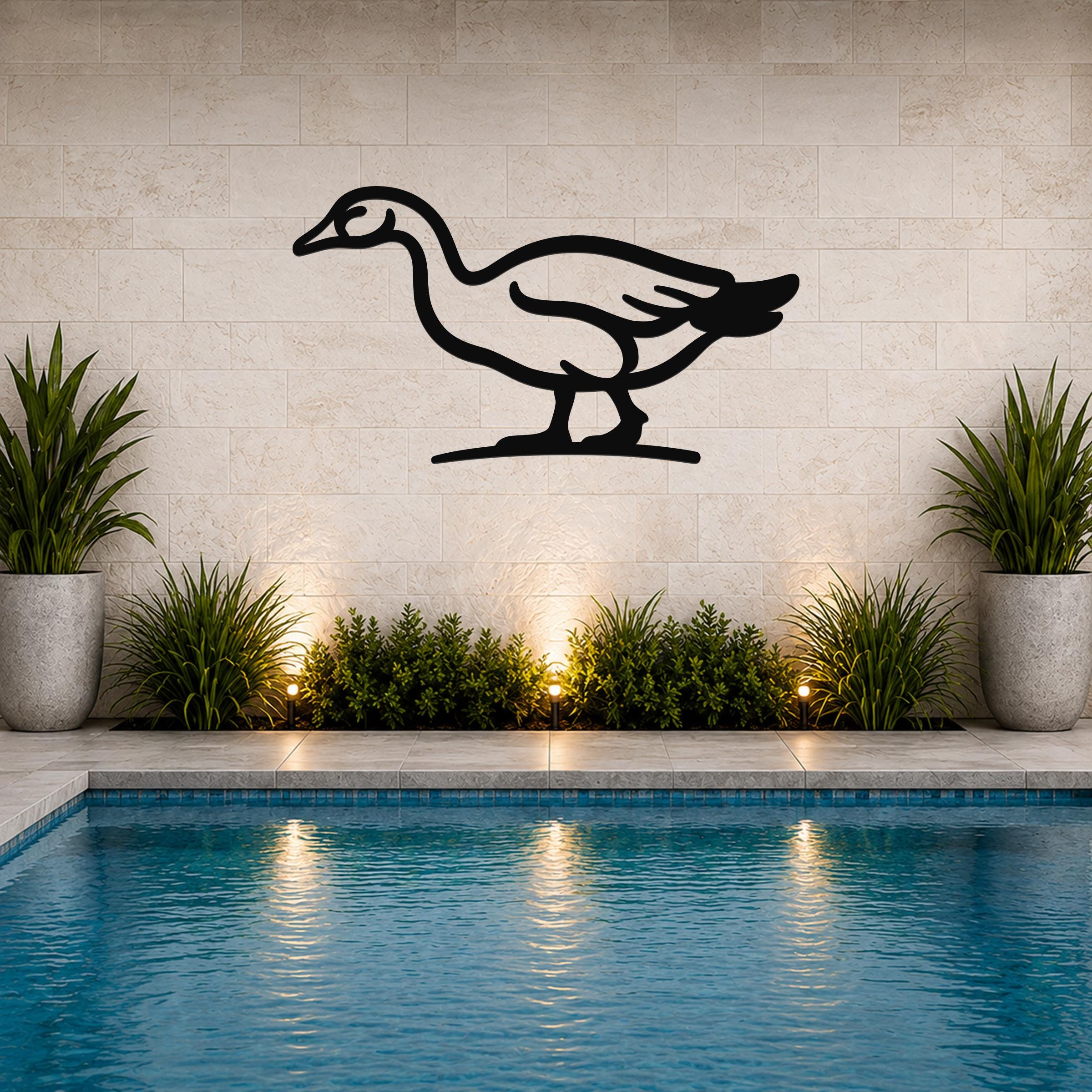 Black metal goose wall art silhouette mounted on a tiled wall above a pool, with potted plants and ground lights below.