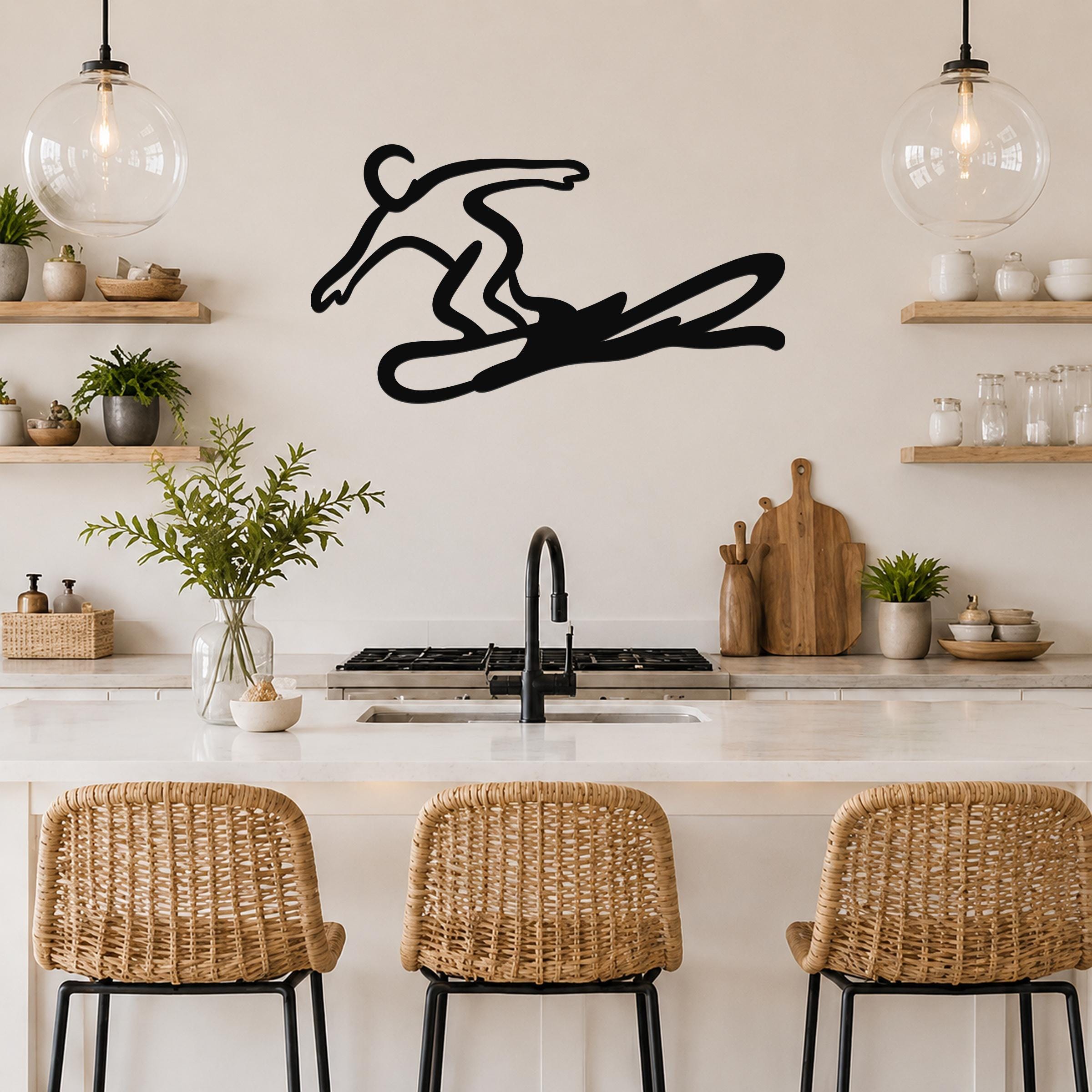 Black metal wall art silhouette of a snowboarder in motion, mounted on a kitchen wall above a counter with wicker bar stools.