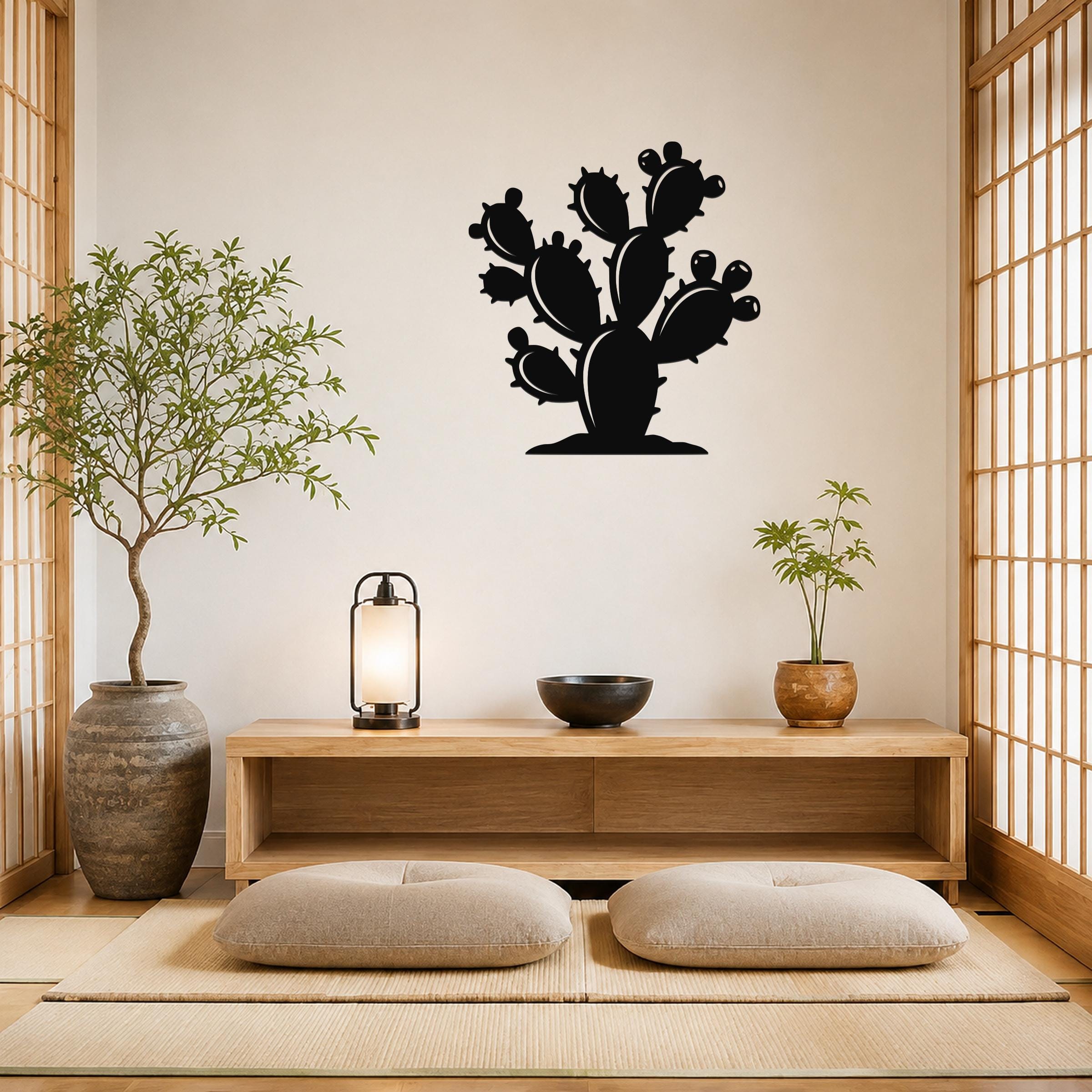 Black metal cactus wall art with multiple paddle-shaped segments and spines, mounted on a light-colored wall above a wooden console in a minimalist room.