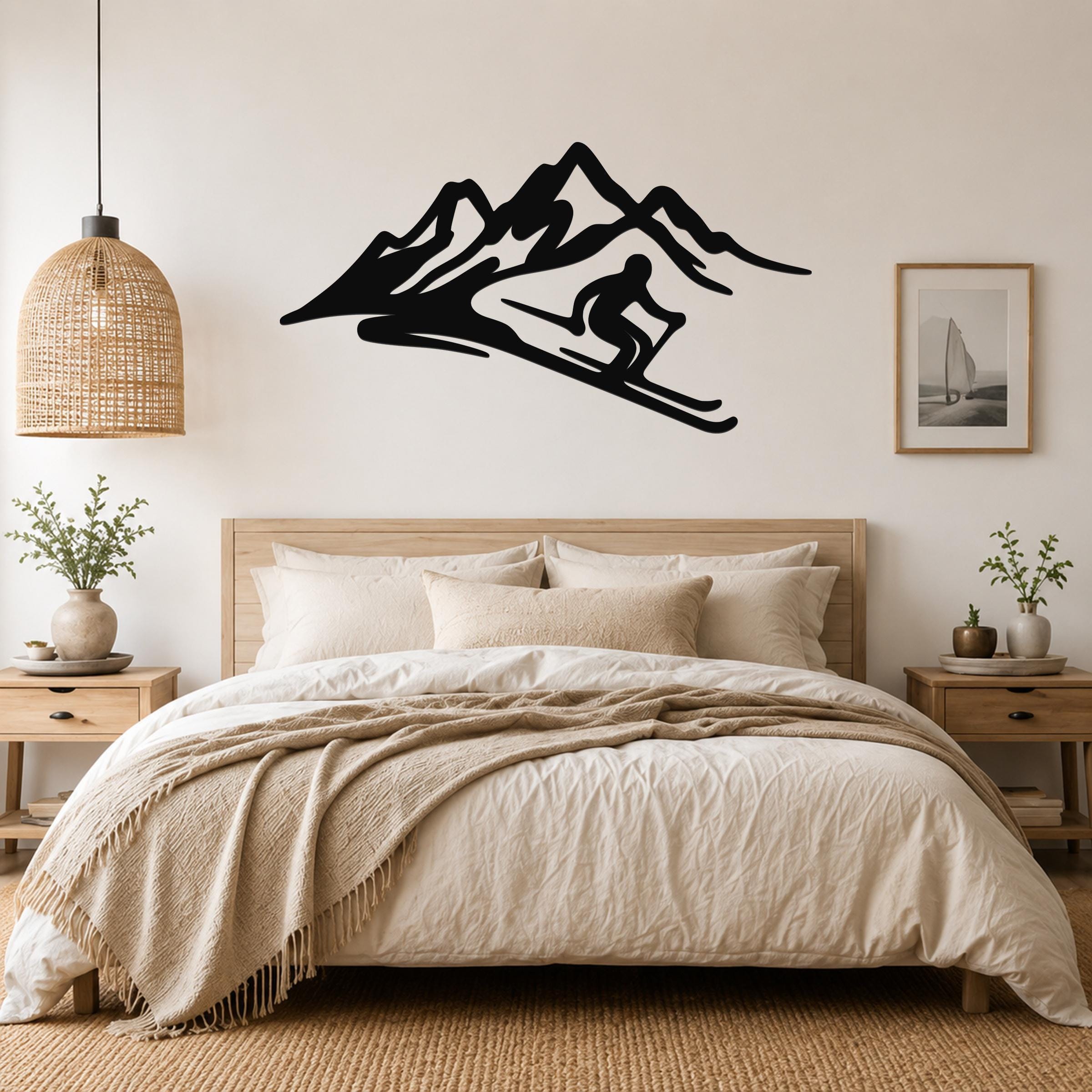 Black metal wall art of a skier in fluid motion on a mountain slope, mounted above a bed in a neutral bedroom.