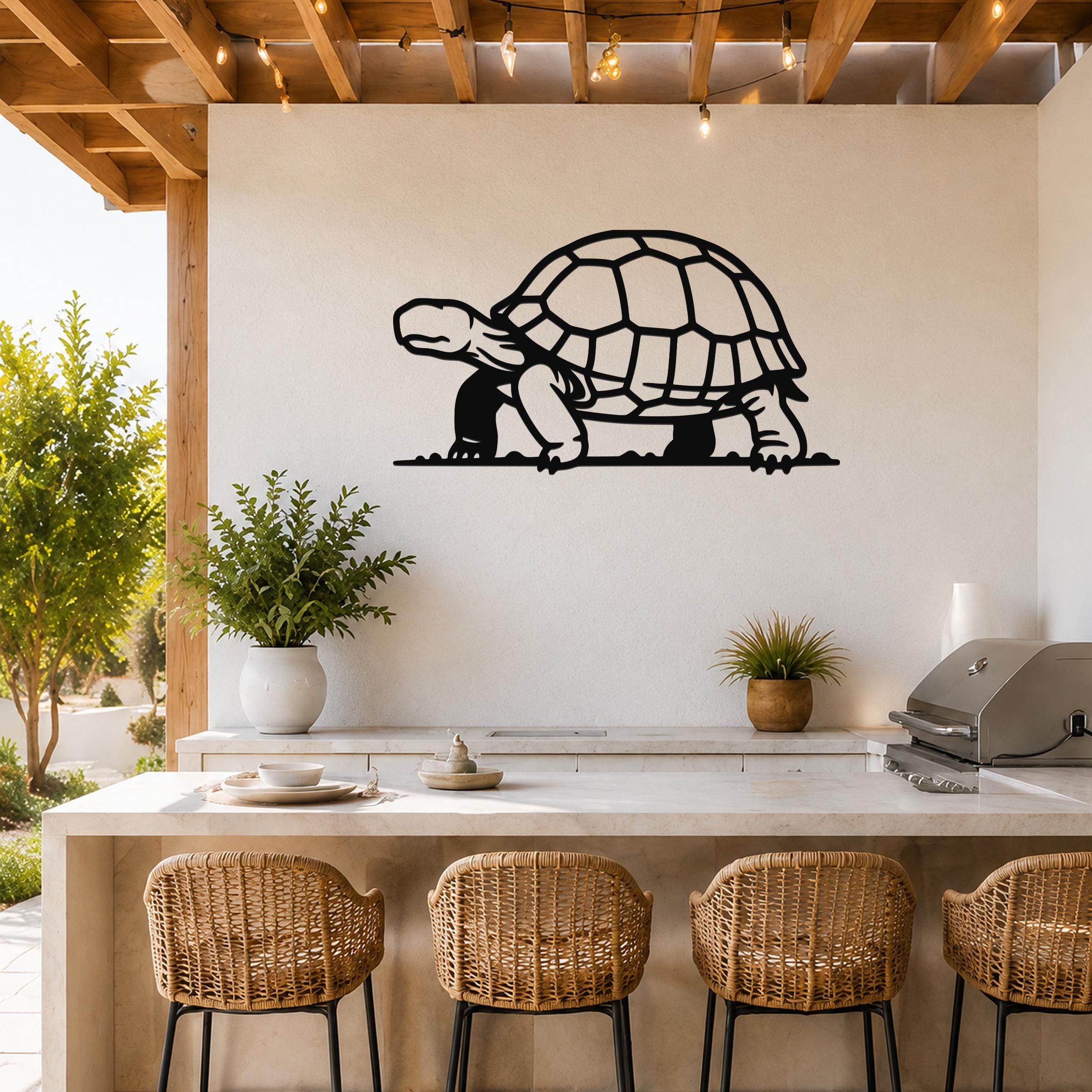 Black metal tortoise wall art with detailed shell cutouts, mounted on a white wall above a kitchen counter with wicker stools.