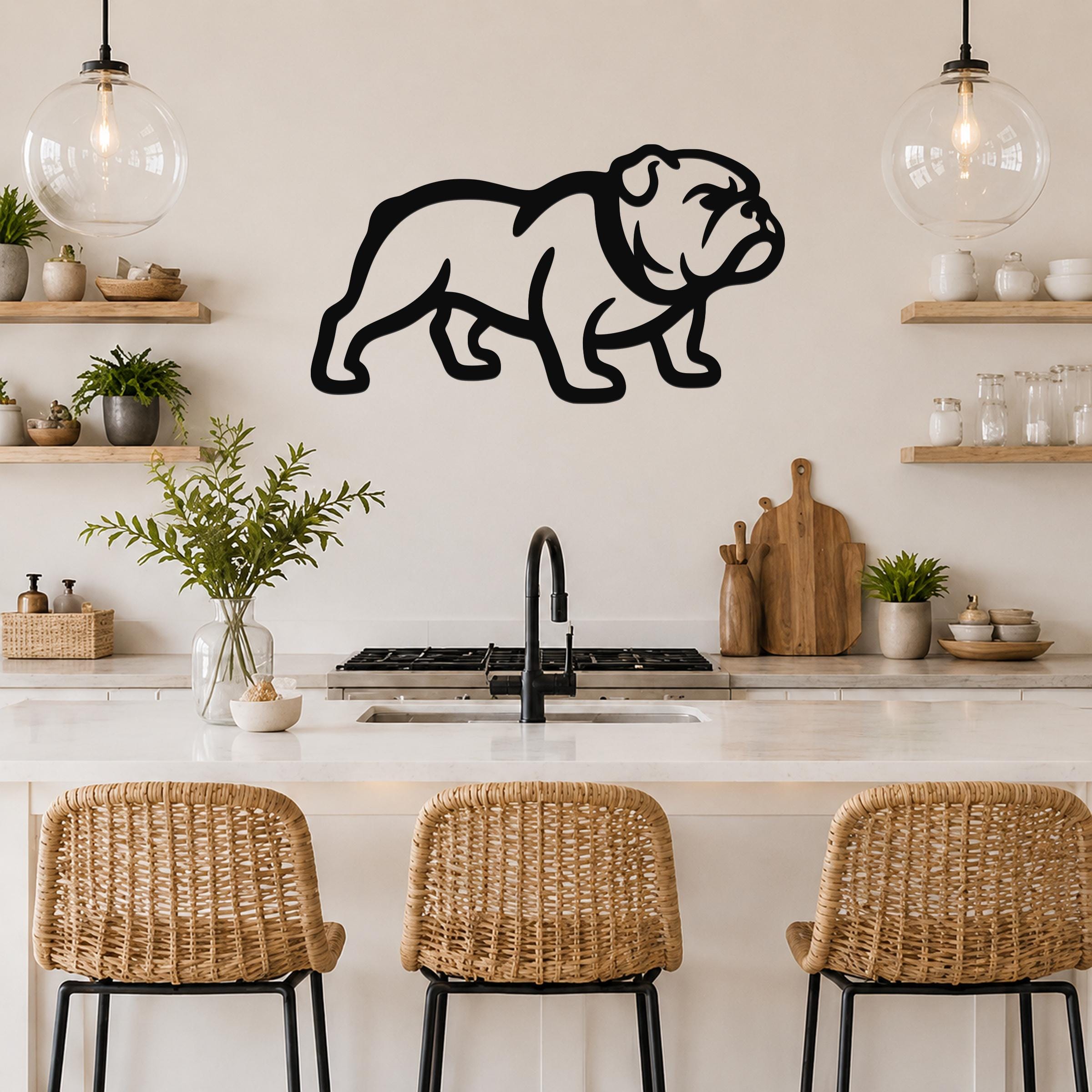 Black metal bulldog wall art silhouette mounted above a kitchen counter, featuring a bold outline of a standing dog with visible internal cutouts, displayed in a modern kitchen with wooden shelves and pendant lights.