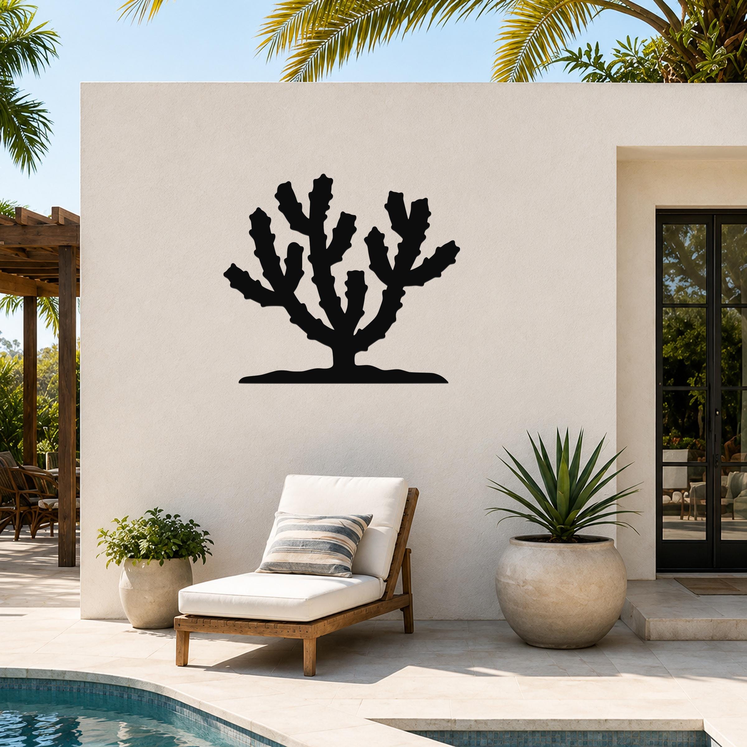 Black metal Cholla cactus wall art silhouette mounted on a white outdoor wall above a lounge chair and potted plants near a pool.