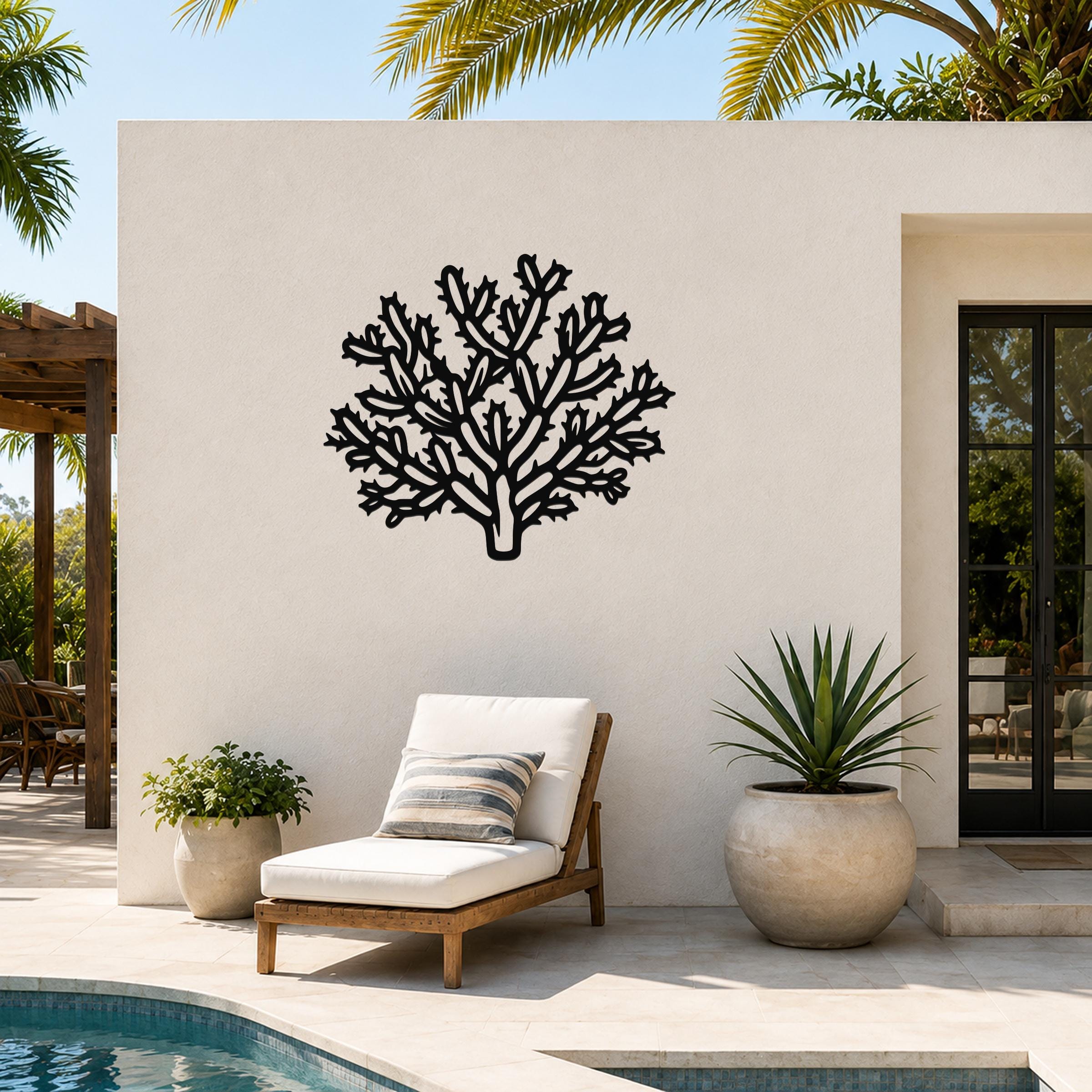 Black metal cholla cactus wall art with intricate branching cutouts, mounted on an outdoor patio wall above a lounge chair.