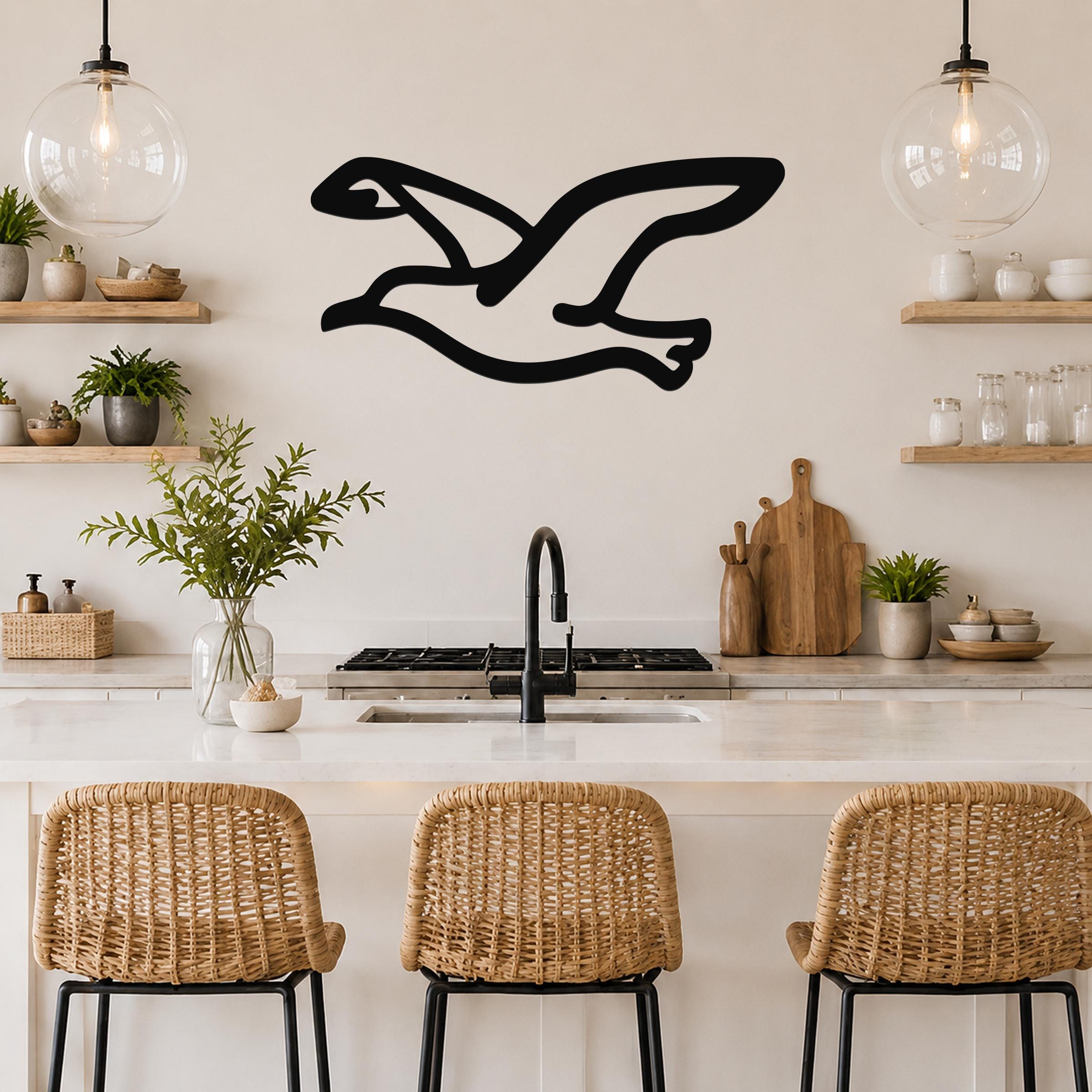 Black metal seagull wall art with a silhouette design, mounted on a kitchen wall above a counter with wicker bar stools.