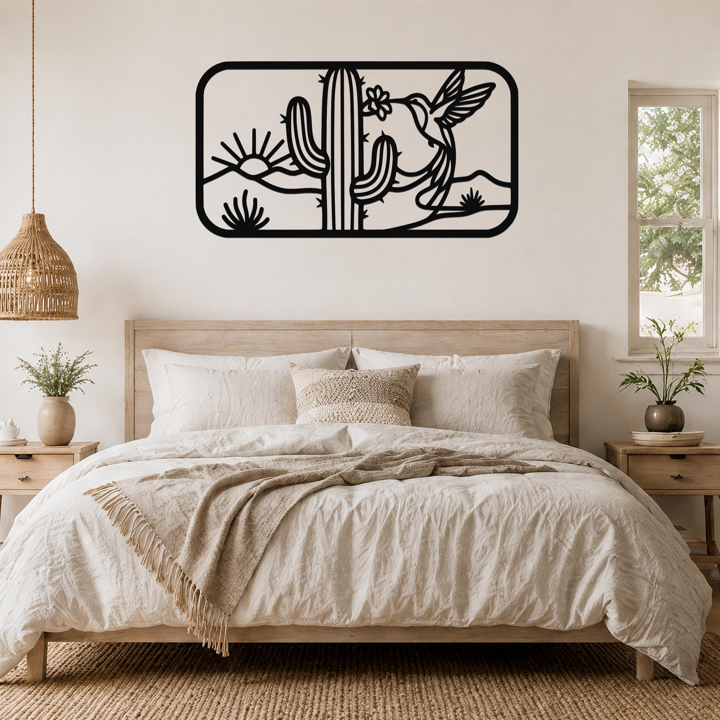 Black metal wall art with a desert scene of saguaro cactus, hummingbird, and sun cutouts, mounted above a bed in a bedroom.